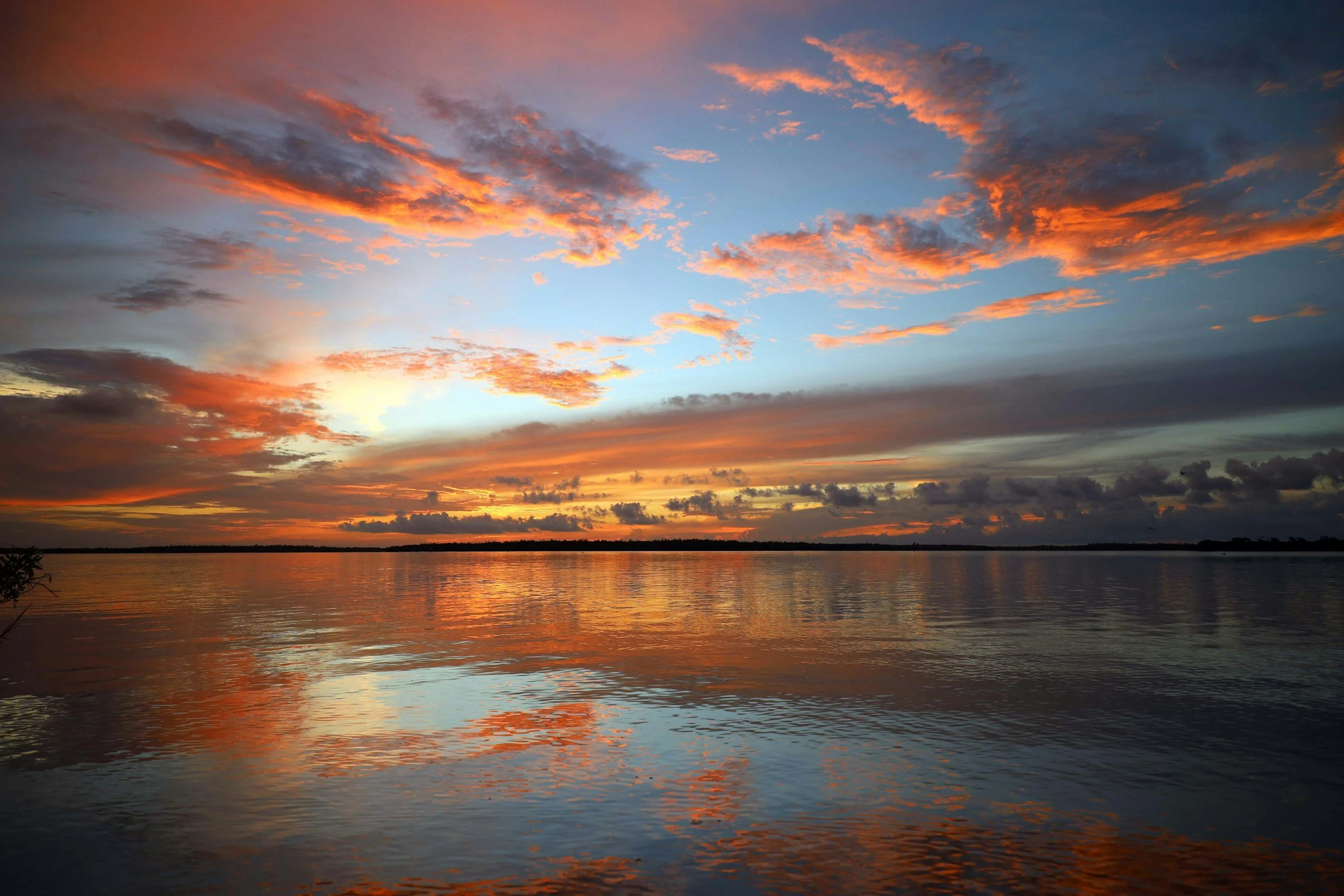 A sunset over a body of water with clouds illuminated in shades of orange and pink in the sky.