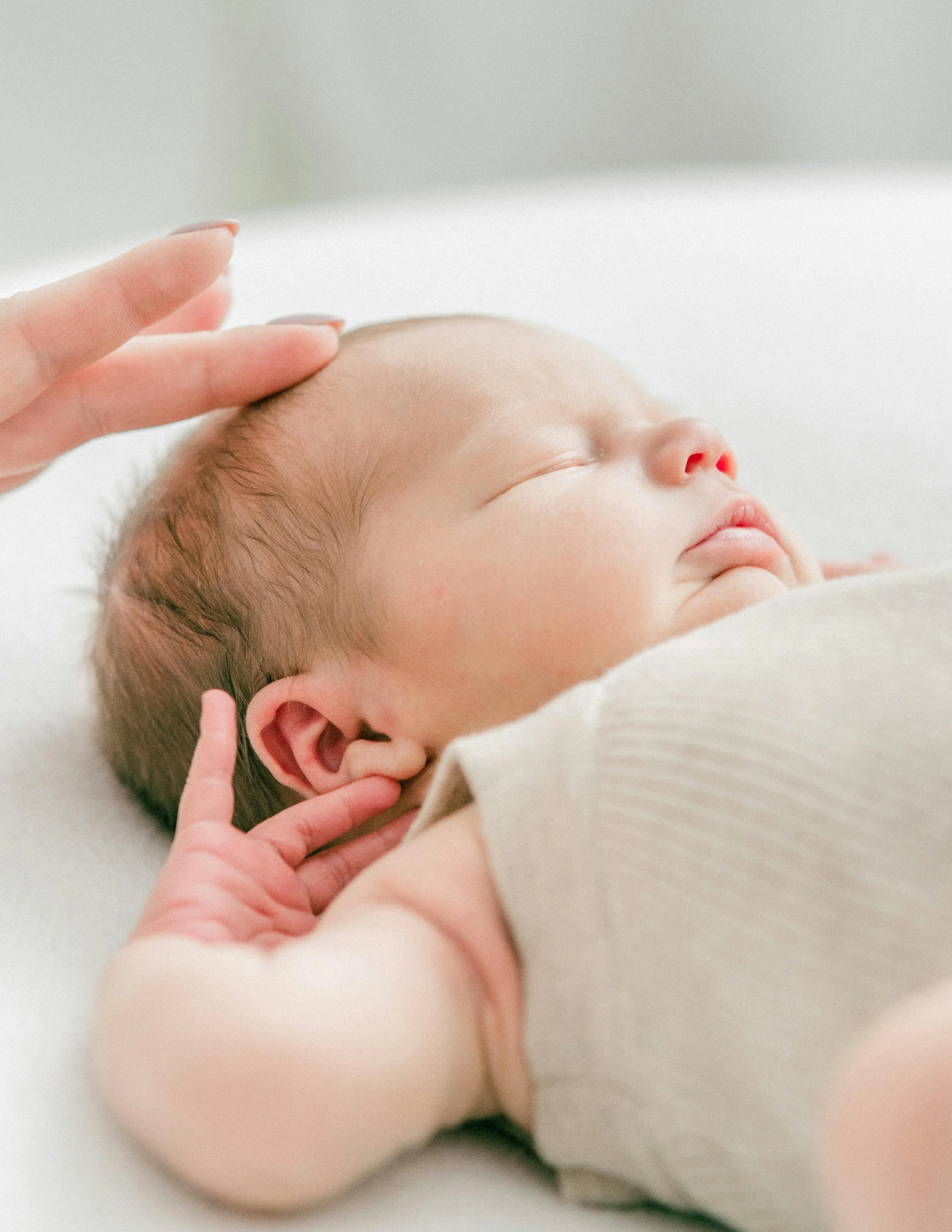 A mother receiving breastfeeding and newborn sleep guidance from The Postpartum Village gently touches her sleeping baby's head in NYC.