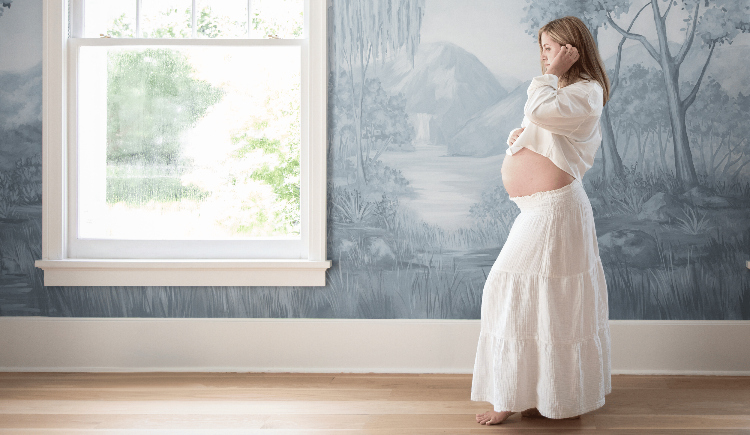 Rachel Bernhard, the founder of the fourth trimester support group The Postpartum Villege, holds her pregnant stomach in a white matching set.