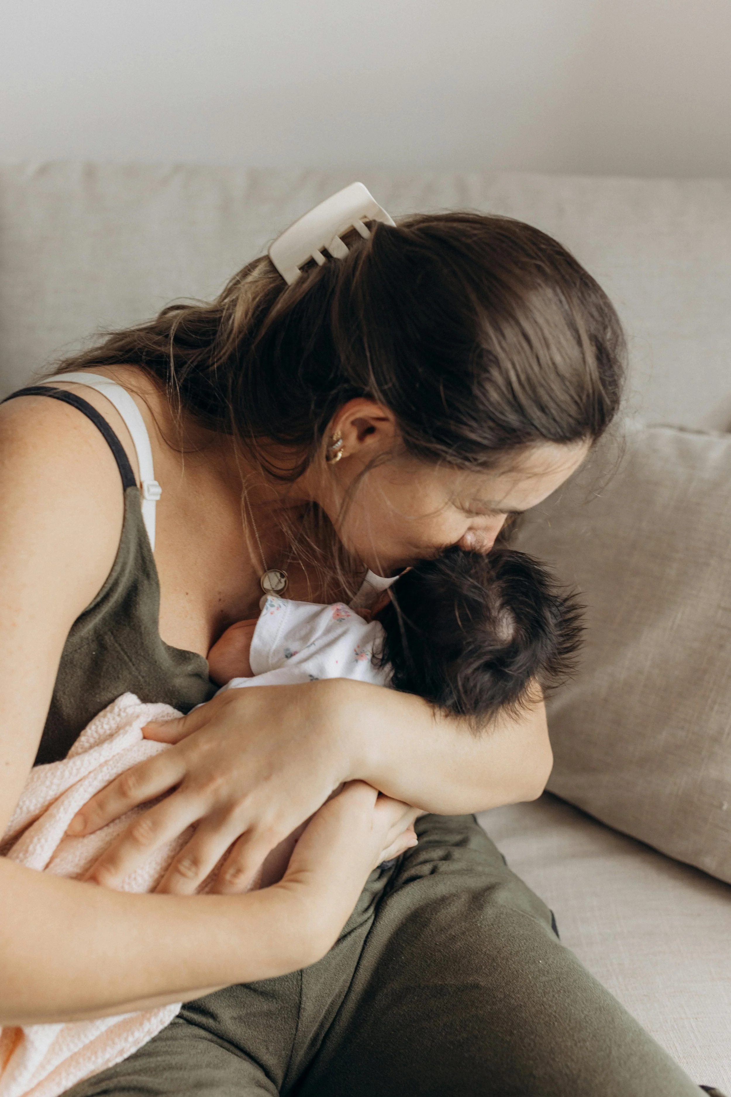 A member of The Postpartum Village kisses her newborn's head, feeling more confident about holistic postpartum support with guidance from her virtual motherhood circle.