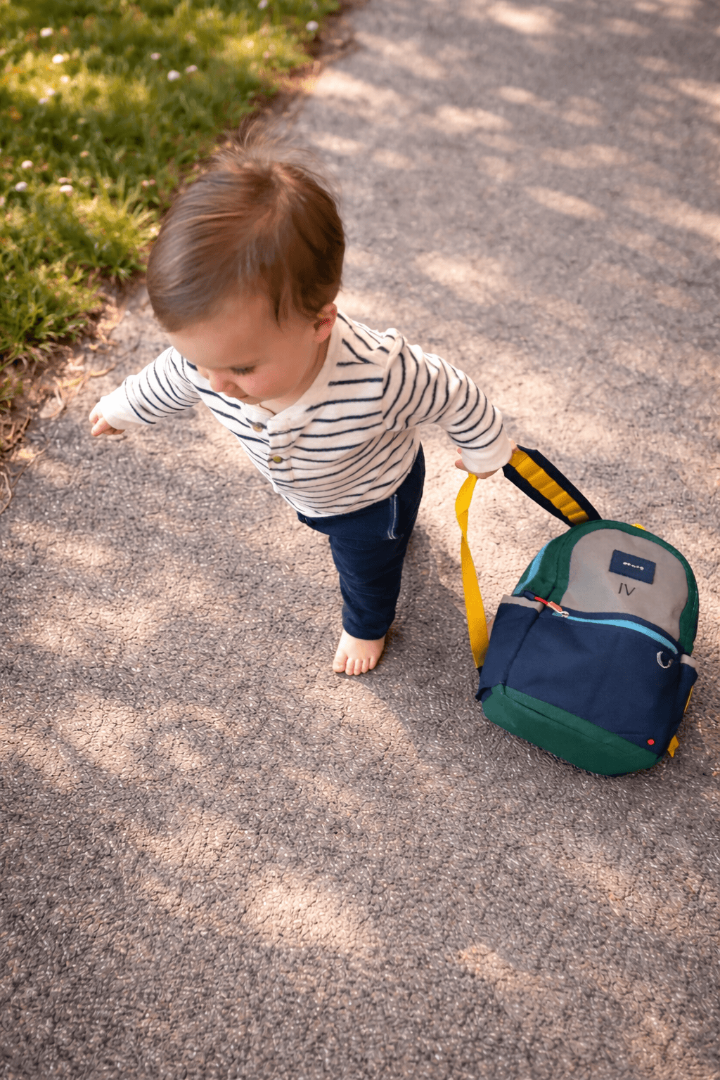 Rachel Bernhard (founder of The Postpartum Village) watches her toddler walking outside holding a backpack.