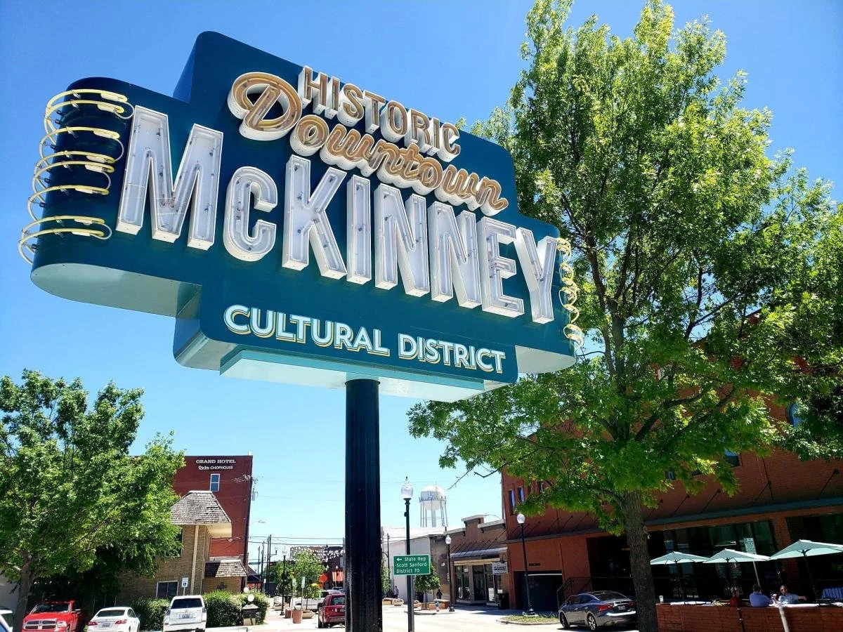Sign for the Historic Downtown McKinney Cultural District with blue sky and trees in the background.