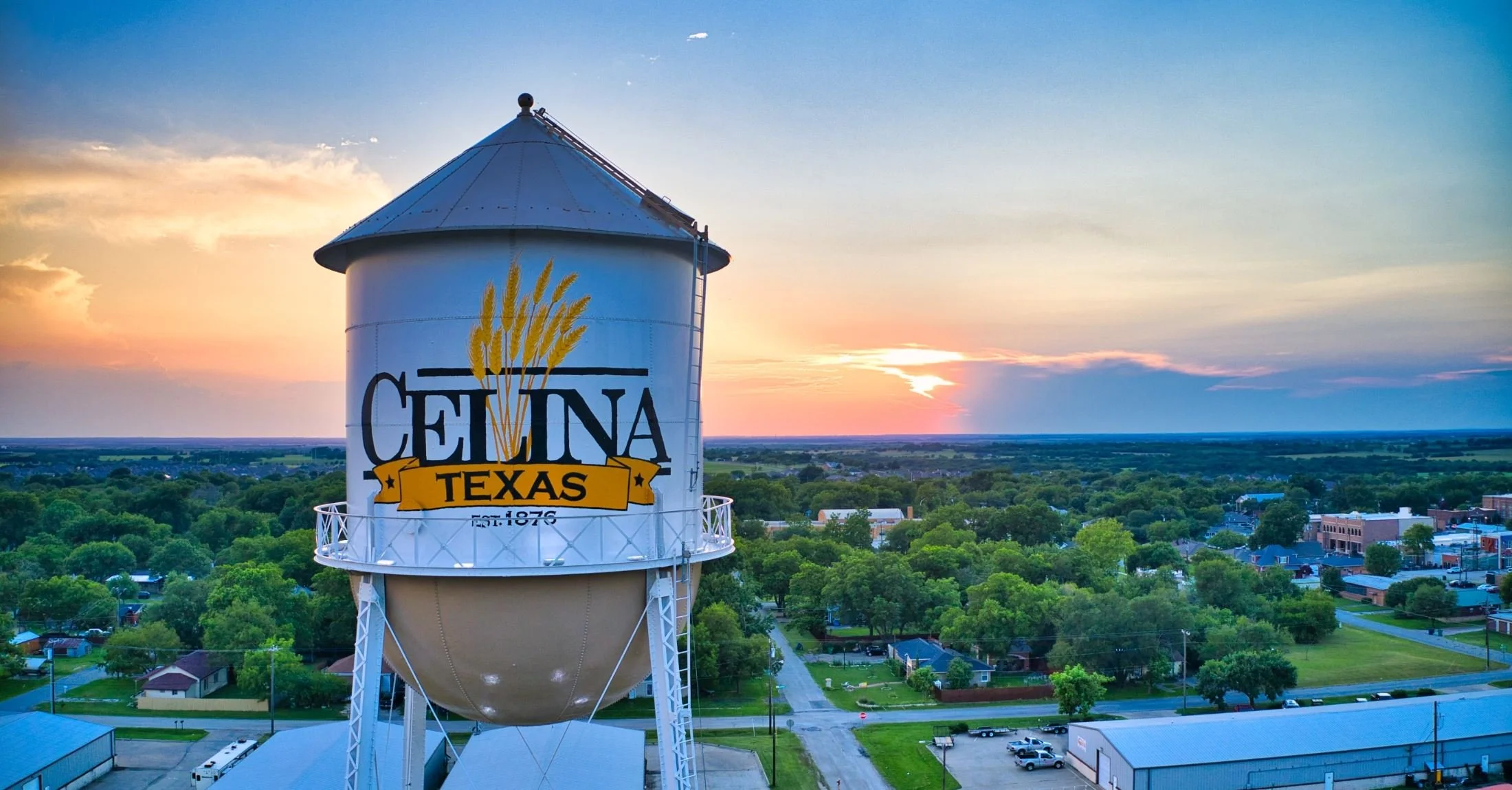 Water tower with Cedarina Texas logo, overlooking a green townscape during sunset.