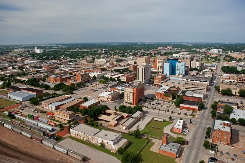 Aerial view of a downtown city with various buildings, streets, and a railway with train cars at the bottom.