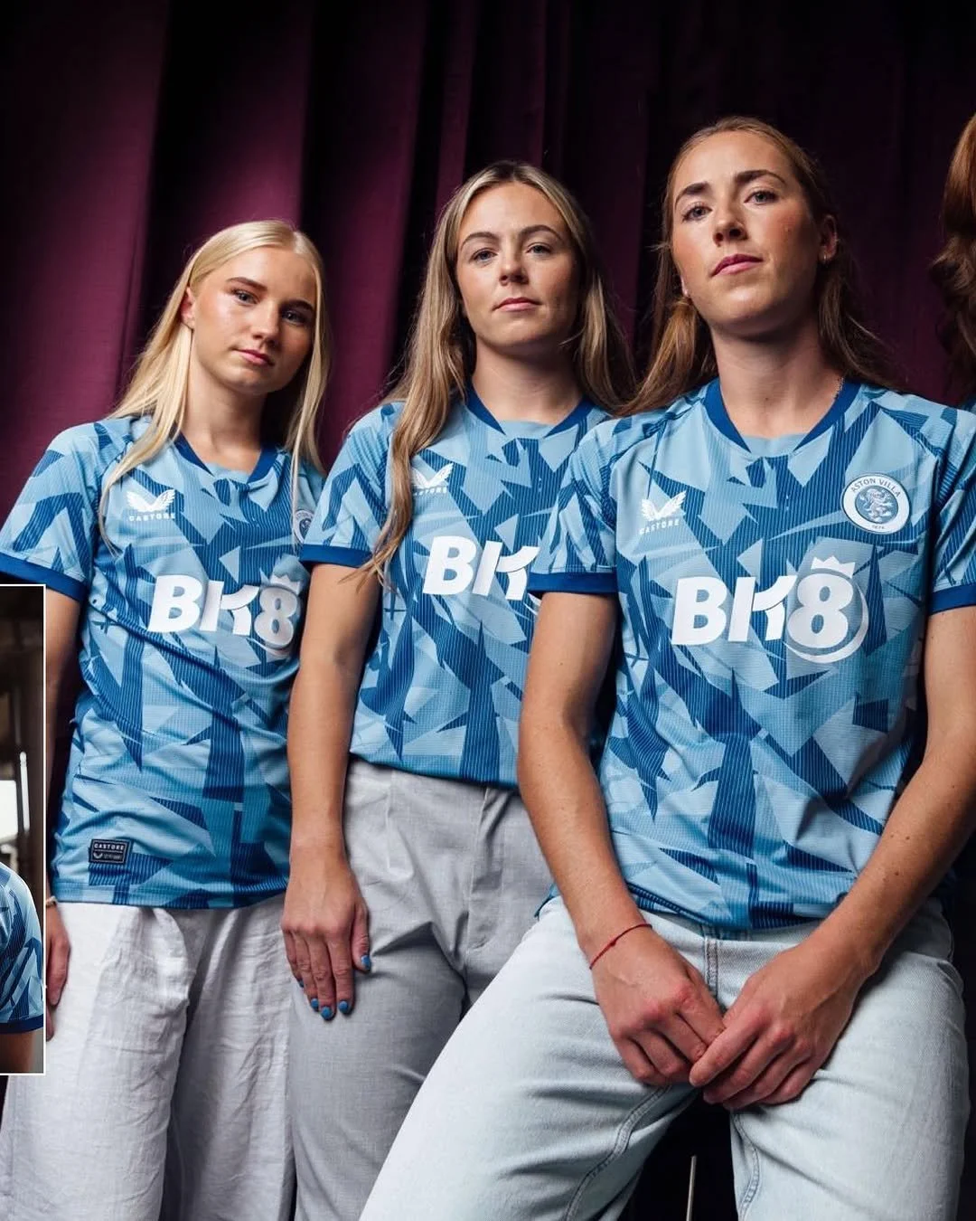 Three young women in matching blue sports jerseys with white and darker blue patterns, standing in front of a purple curtain, looking serious.
