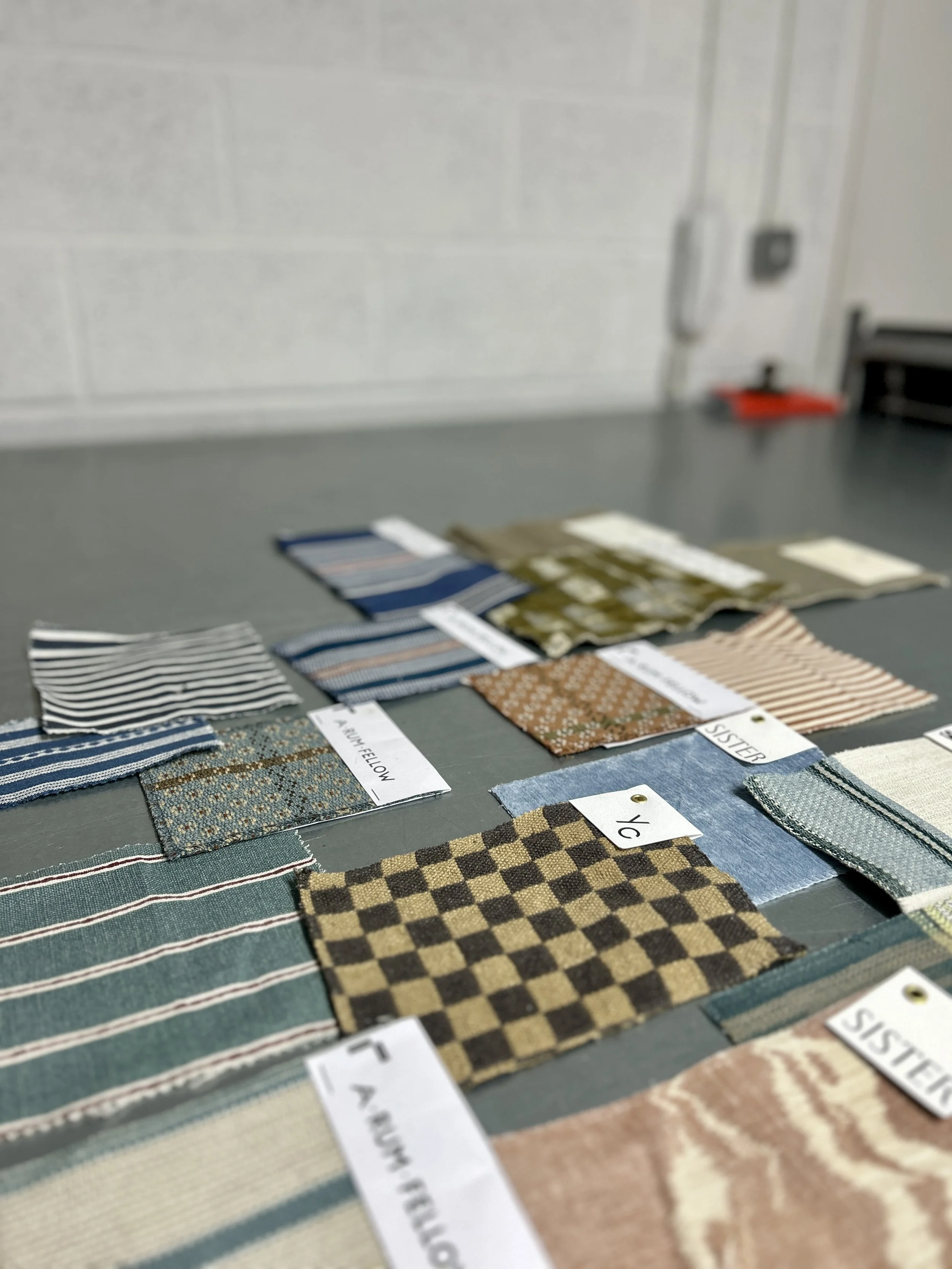 Display of fabric swatches with various patterns and colours, from Yarn Collective, A Rum Fellow, Helene Blanche and others arranged on a table with labels. Just a selection of the fabrics Hayward Studio Upholstery are able to supply to their clients