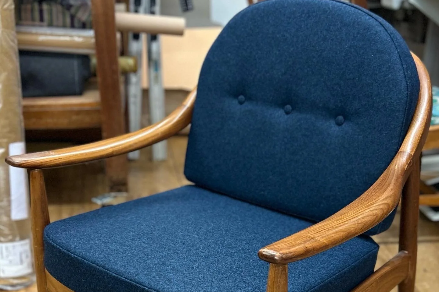 Wooden armchair with blue fabric upholstery, rounded backrest, and two decorative buttons on the backrest in a furniture store.