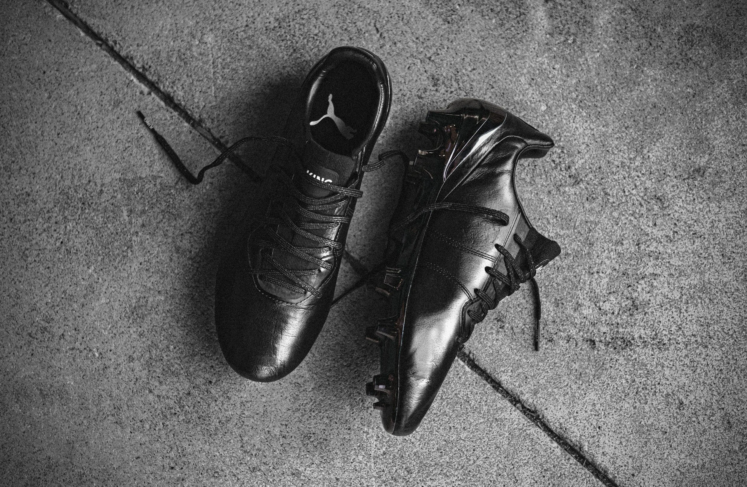 A pair of black Nike high-top sneakers with black laces are placed on a dark, textured concrete floor.