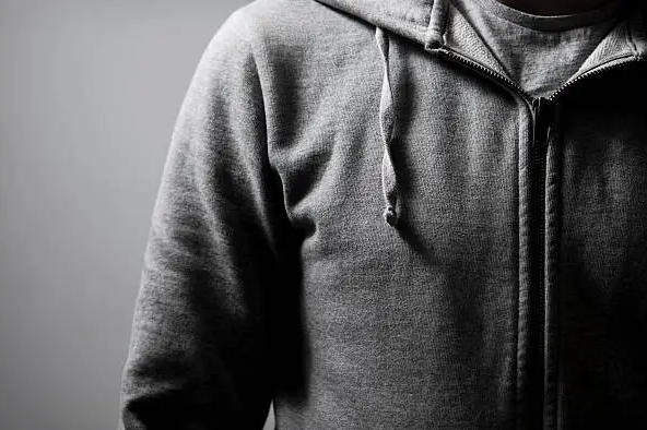 Close-up of a person wearing a gray hooded sweatshirt with the zipper partially zipped up.