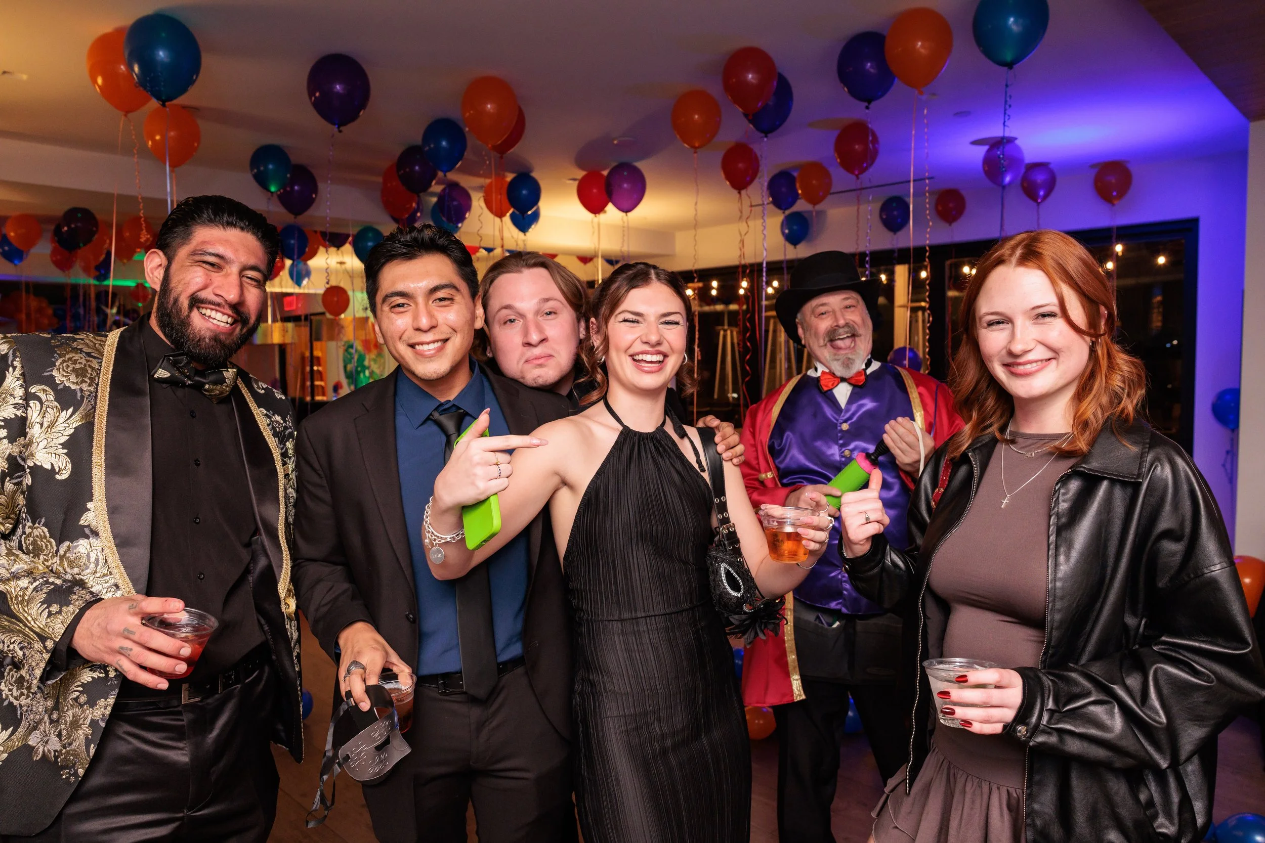 People celebrating at a party with colorful balloons and decorations, holding drinks and smiling.