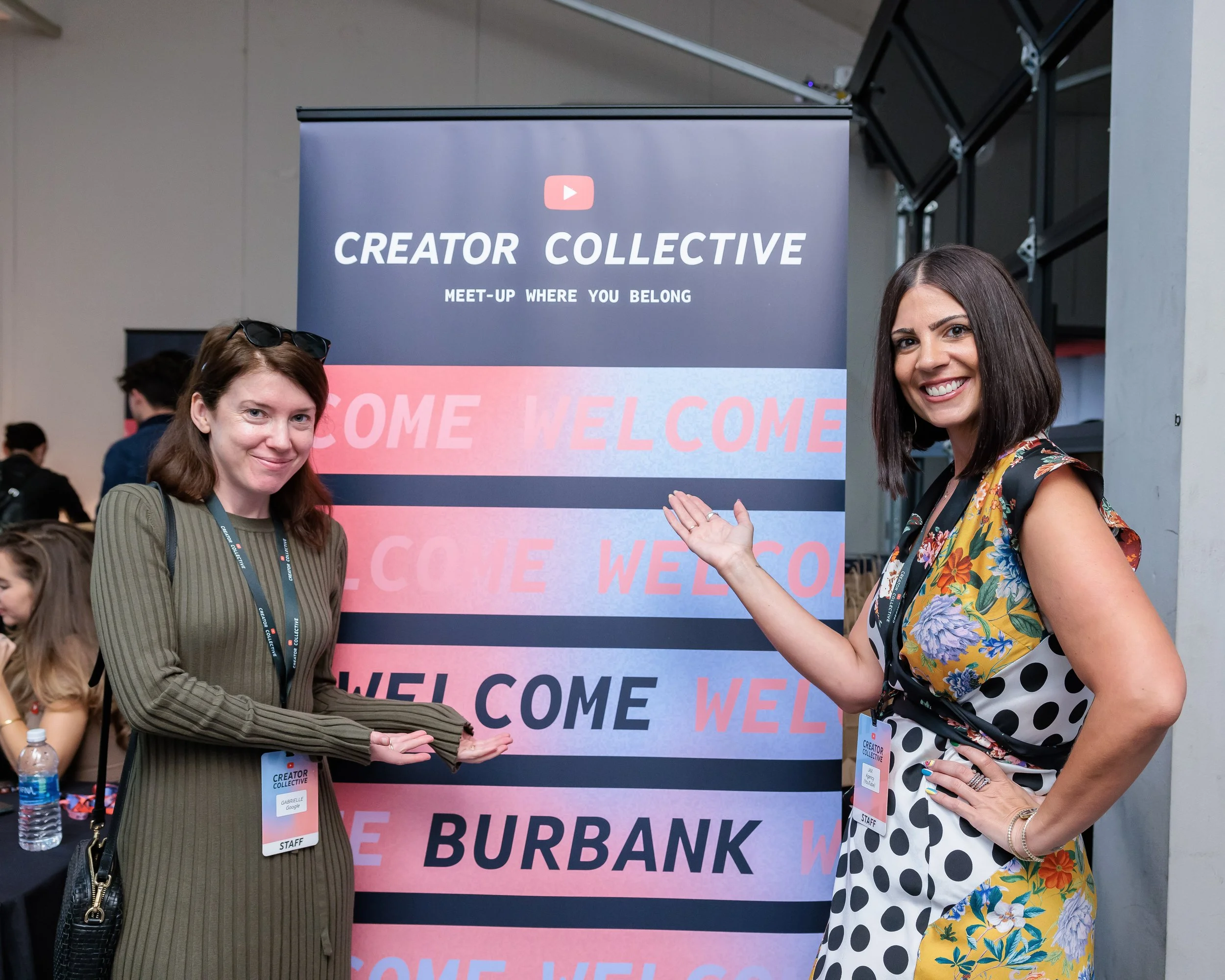 Two women standing next to a sign at the Creator Collective event in Burbank, smiling and posing for the photo.
