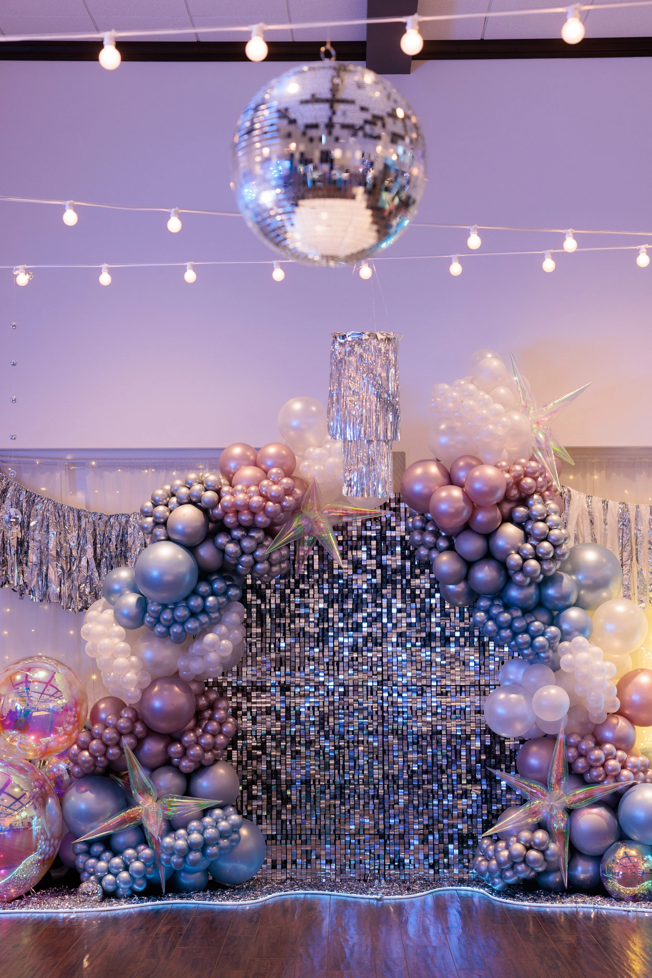 Decorative backdrop with balloons, a disco ball, and shimmering silver decorations for a celebration or party.