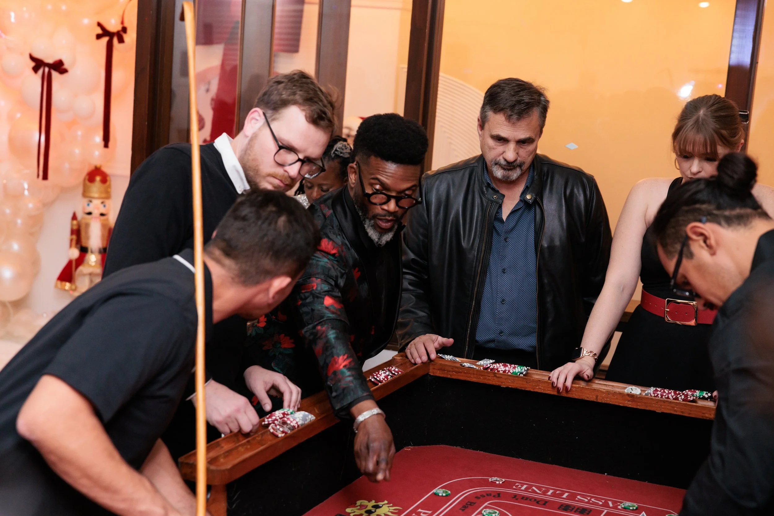 Group of people gathered around a roulette table playing a game at a festive event, decorated with balloons and nutcracker figures.