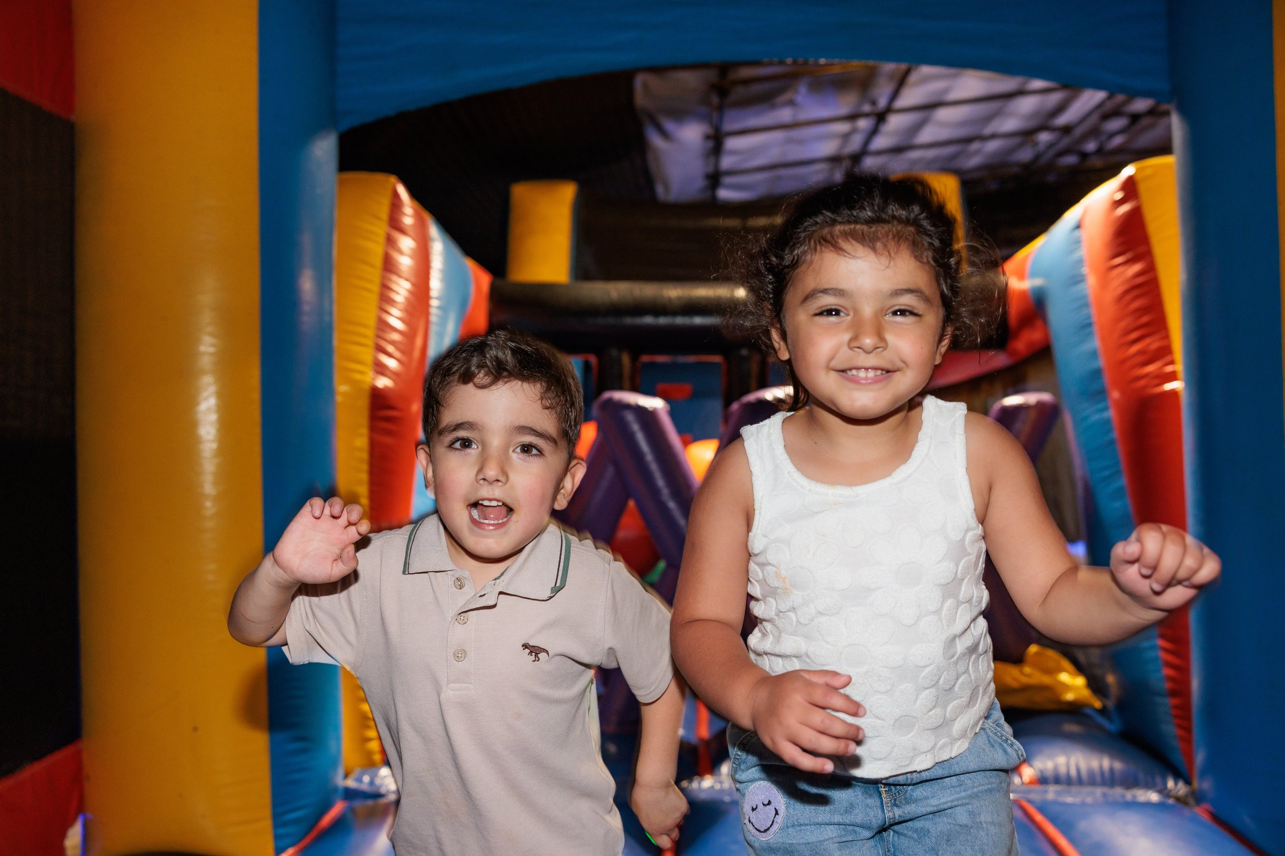 Two young children, a boy and a girl, smiling and playing on an inflatable bounce house.