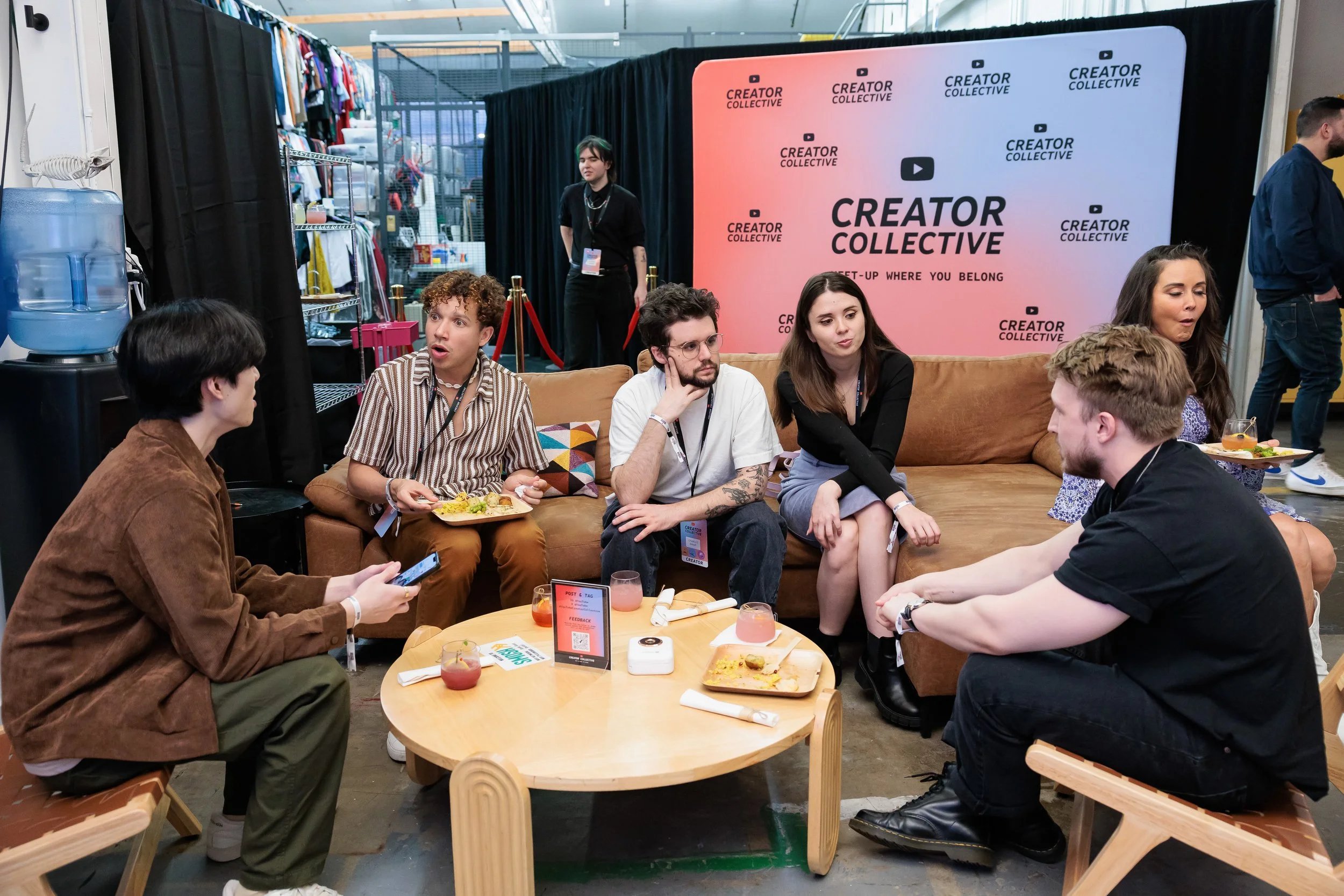 Group of people sitting on a couch and chairs, engaging in conversation at a Creator Collective event, with food and drinks on a small table in front of them.