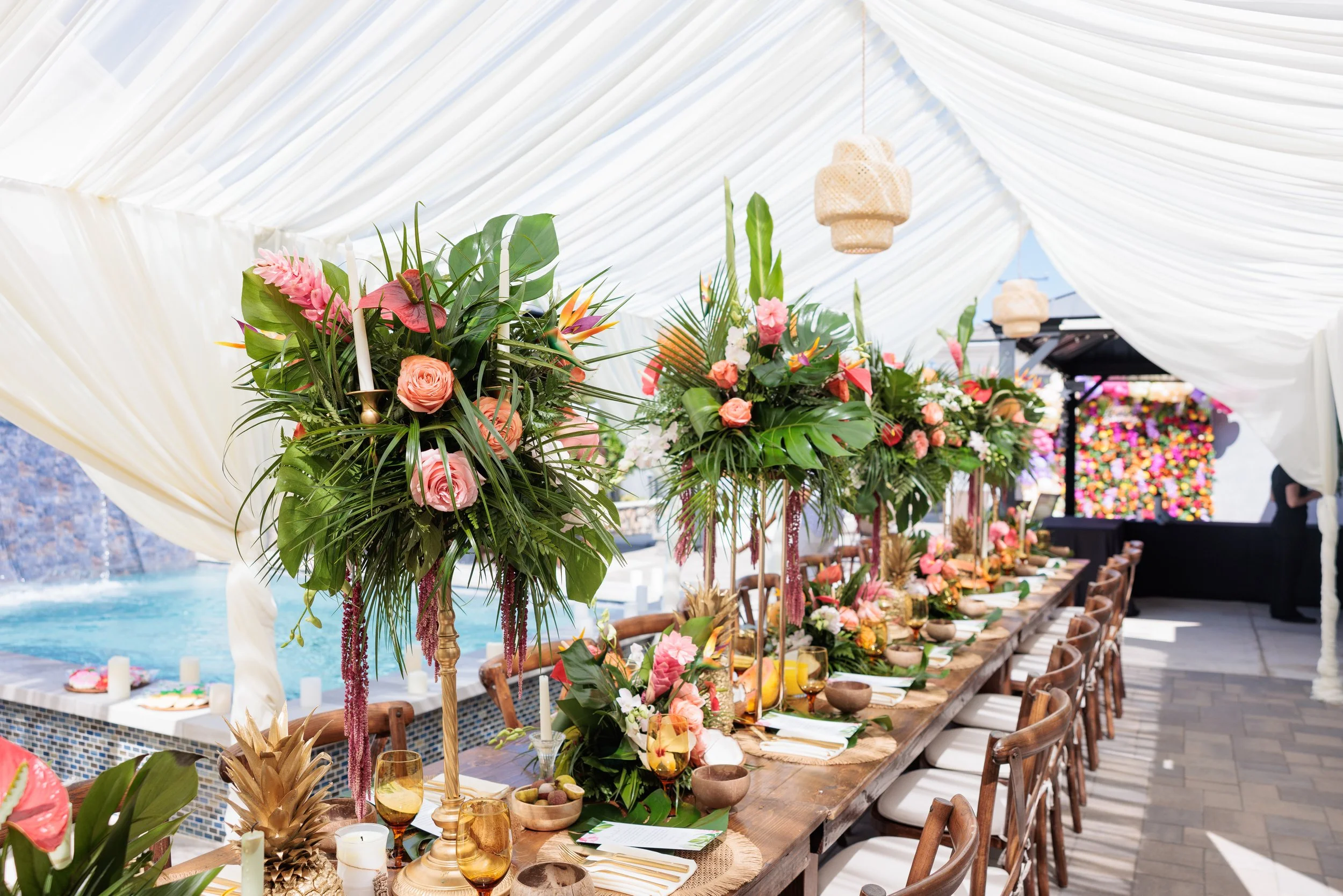 Decorated long dining table with floral centerpieces under a white tent at an outdoor event.