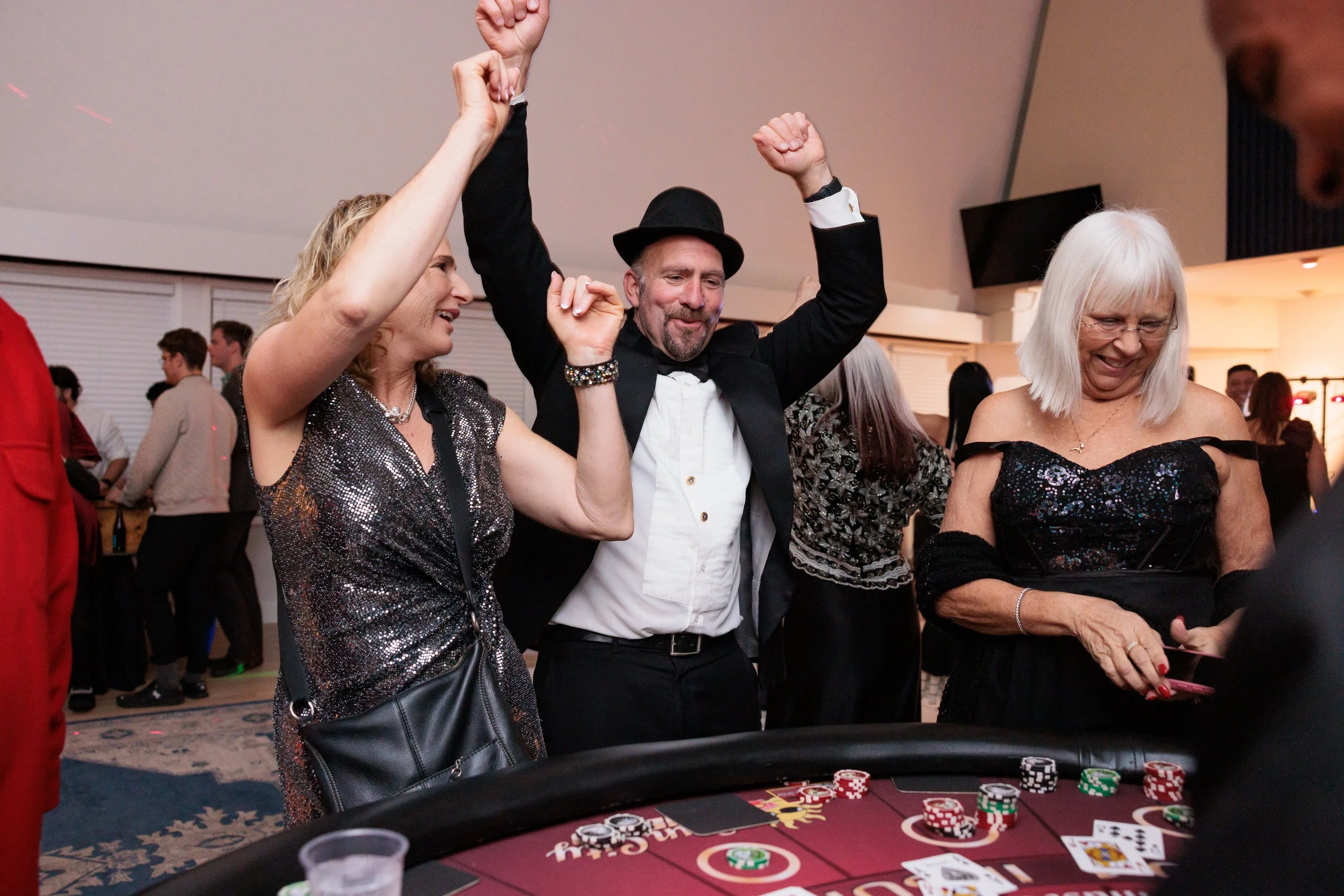People celebrating at a casino table, with a woman and a man in formal attire, raising their hands in victory.