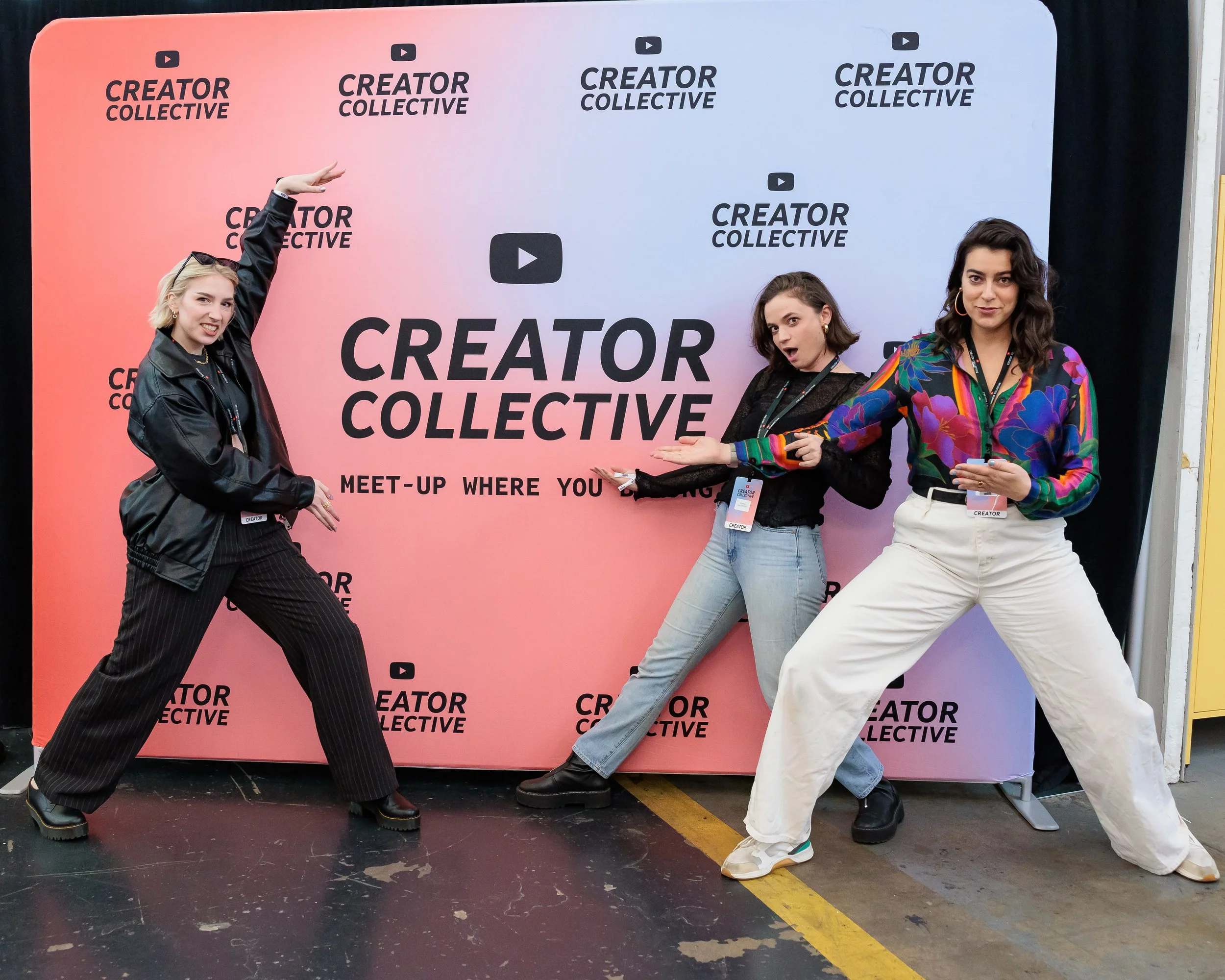 Three women posing in front of a backdrop that says "Creator Collective" and "Meet-up where you" with journalists lanyards around their necks. They are making dynamic gestures and smiling.
