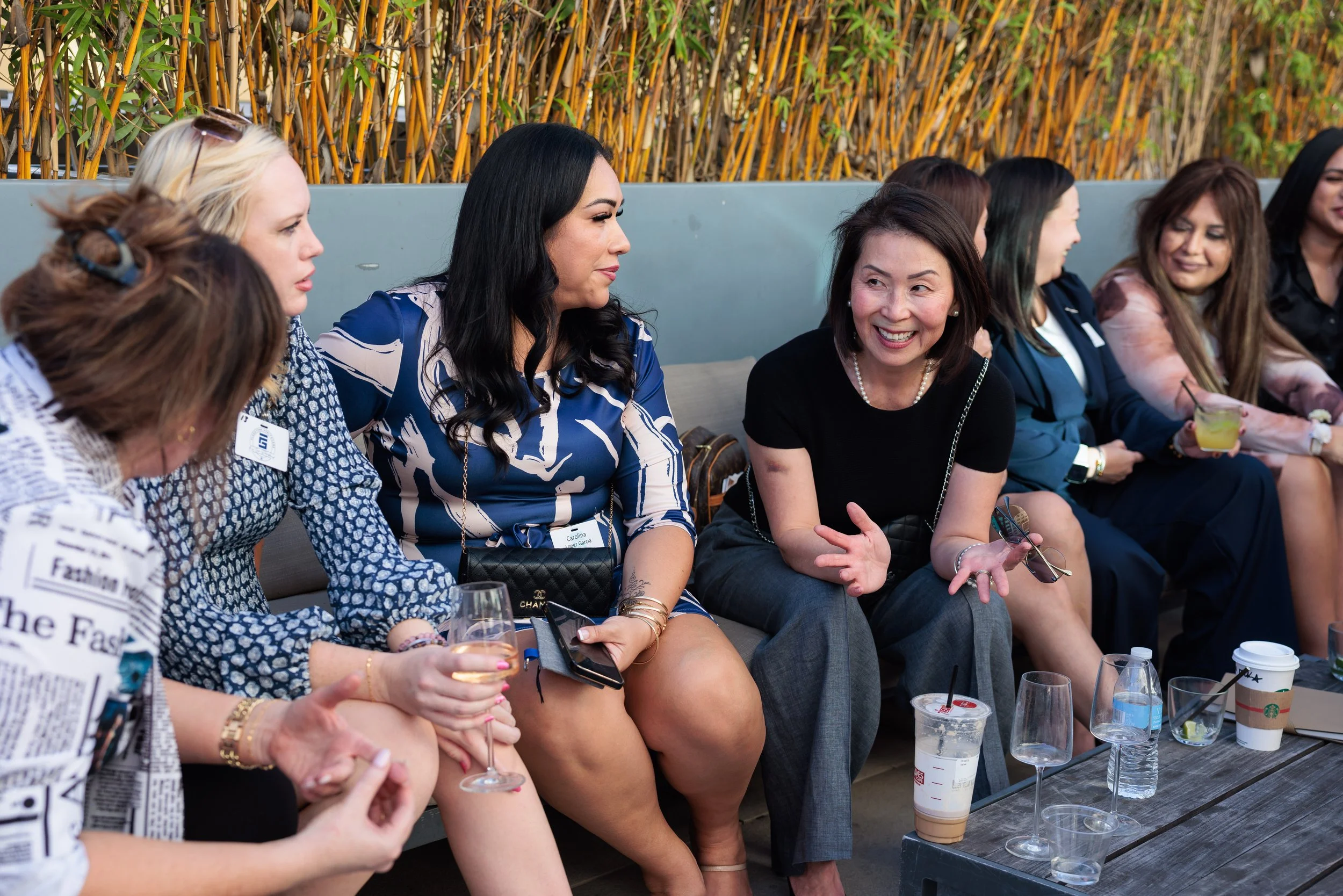 Group of women sitting and chatting at an outdoor social event, with drinks on the table in front of them.