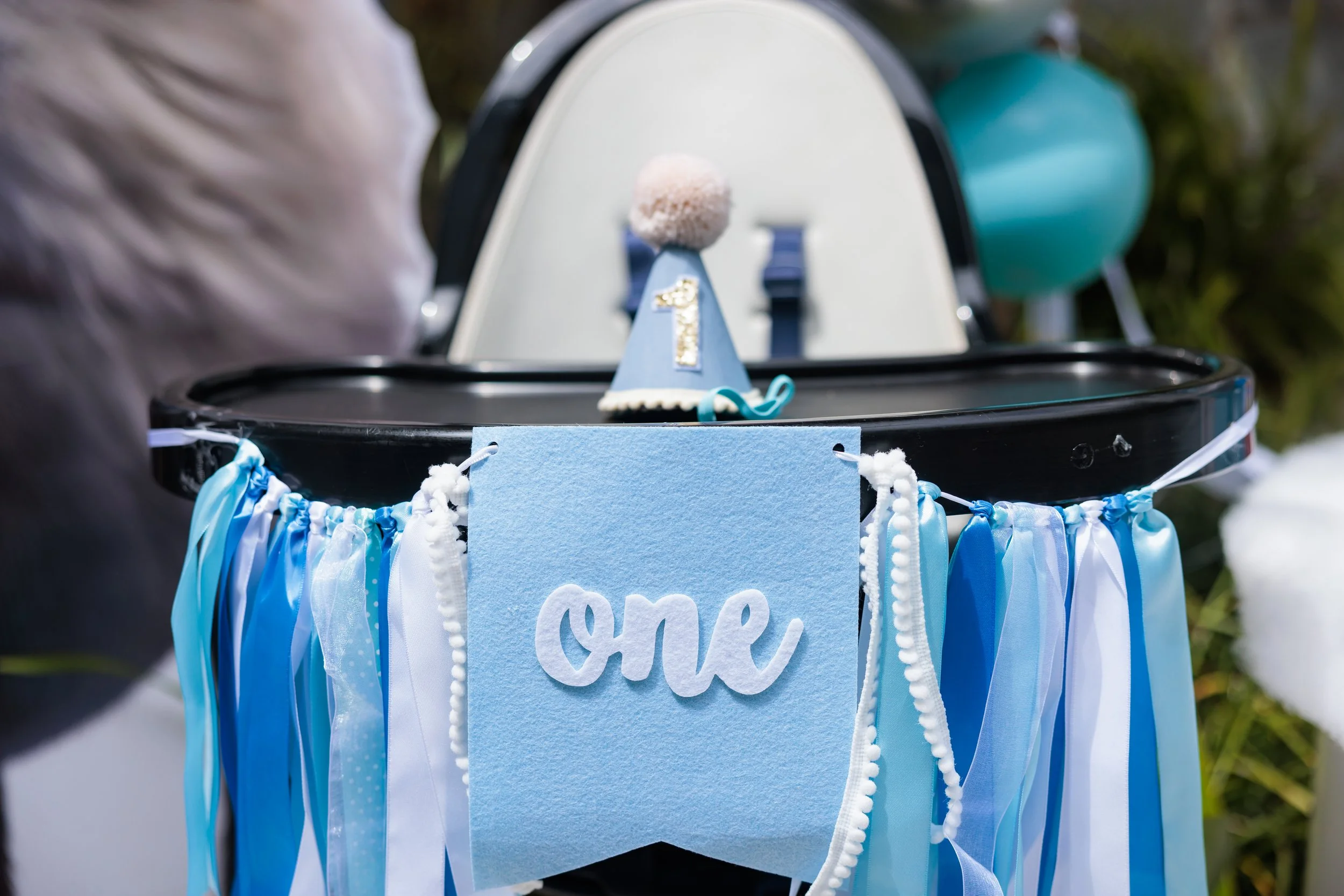 Celebration setup with blue and white decorations, a blue felt banner with the word "one" and a birthday hat with the number 1 on it, likely for a first birthday party.