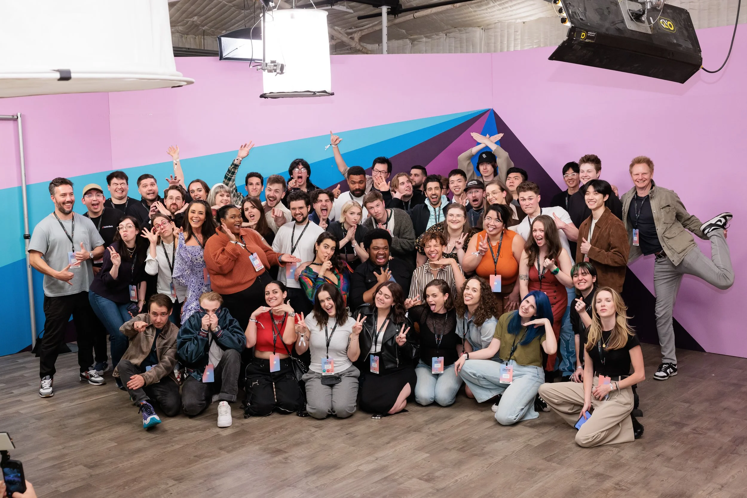 Group photo of a diverse crowd of people smiling and posing in a colorful, modern indoor setting with a purple and blue geometric mural on the wall behind them.