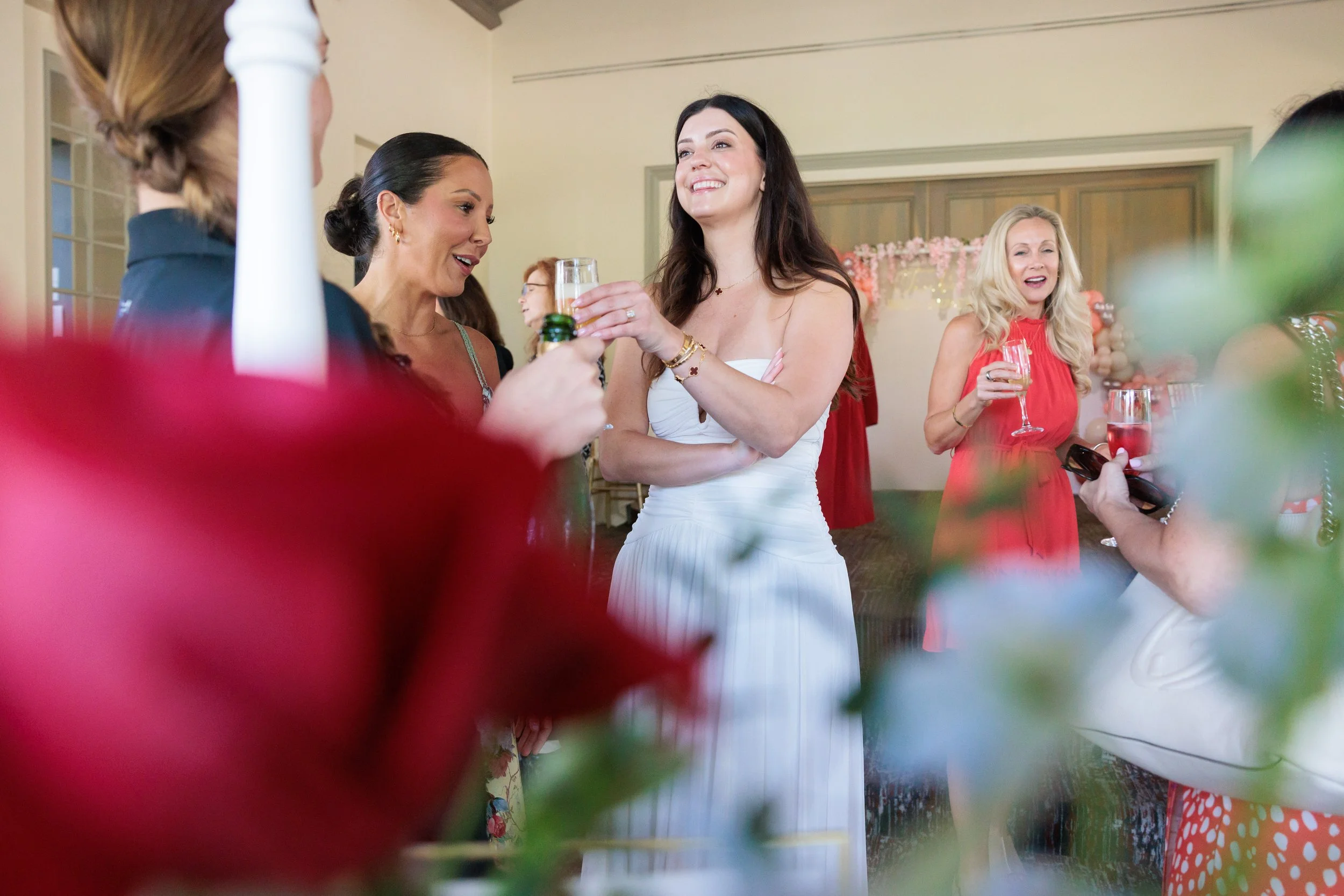 Women at a celebration socializing, holding drinks, and smiling indoors.
