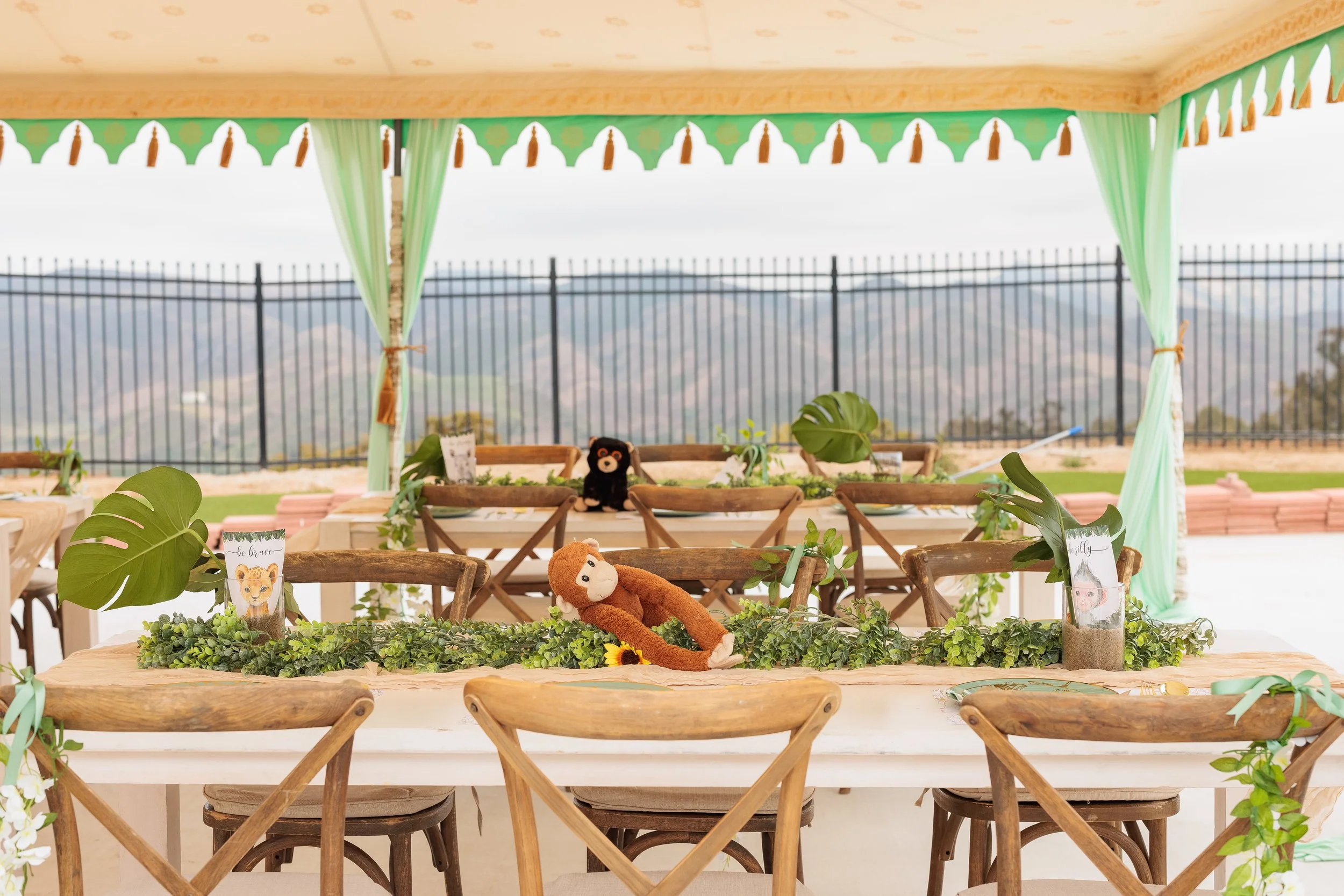 Outdoor banquet table decorated with plush toys and greenery, with a scenic mountain view in the background.