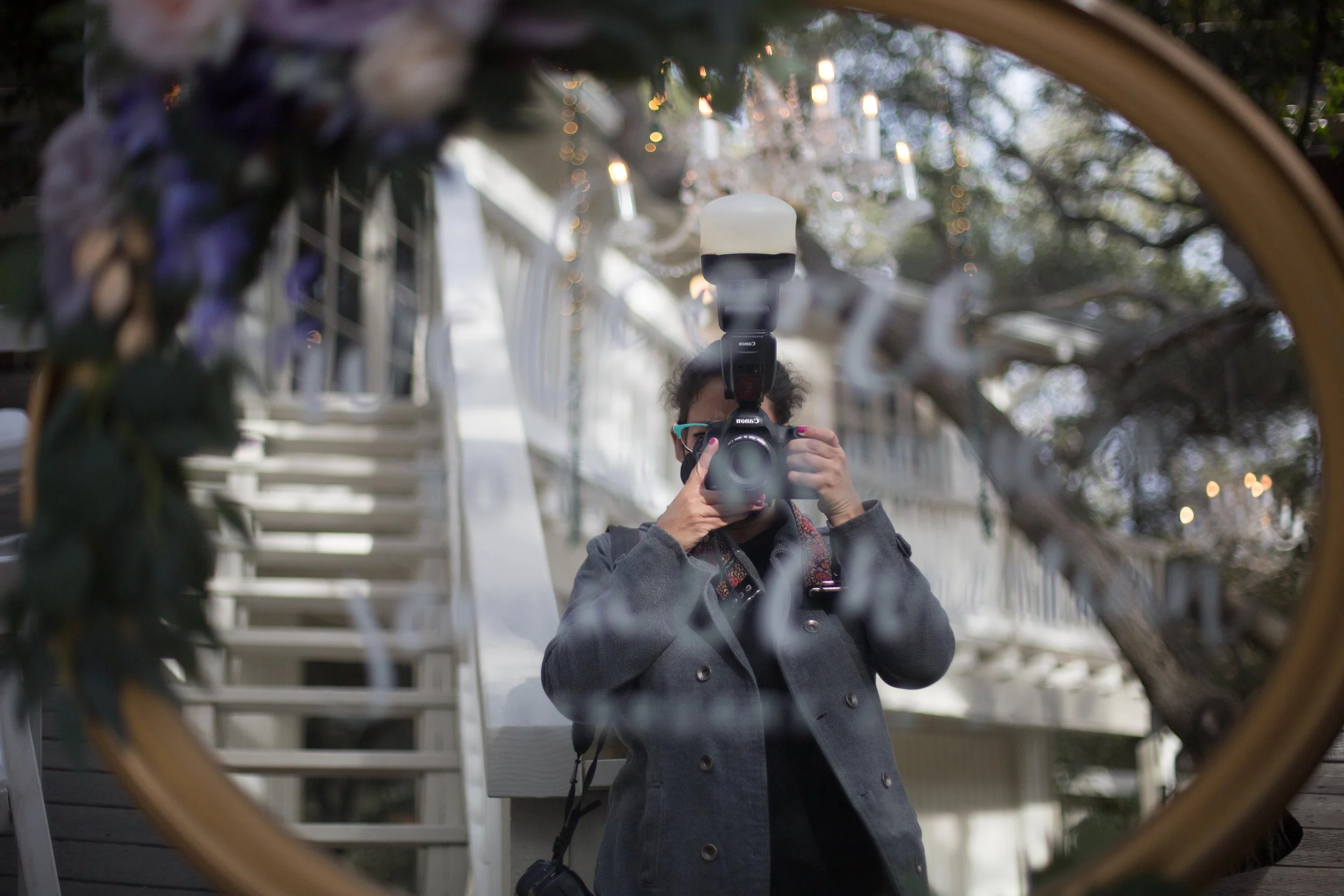 Person taking a photo of herself in a round mirror outdoors, with trees and buildings in the background.