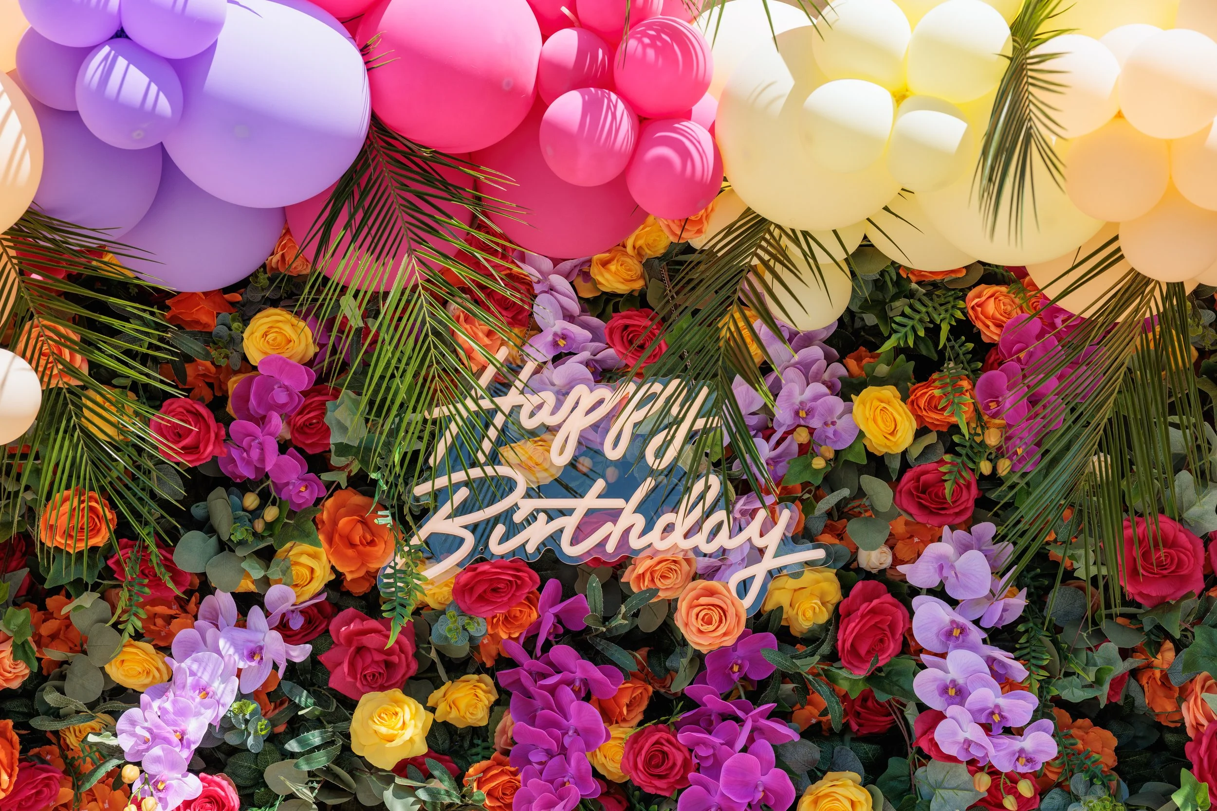 Colorful balloon and flower display with a 'Happy Birthday' sign in the center.