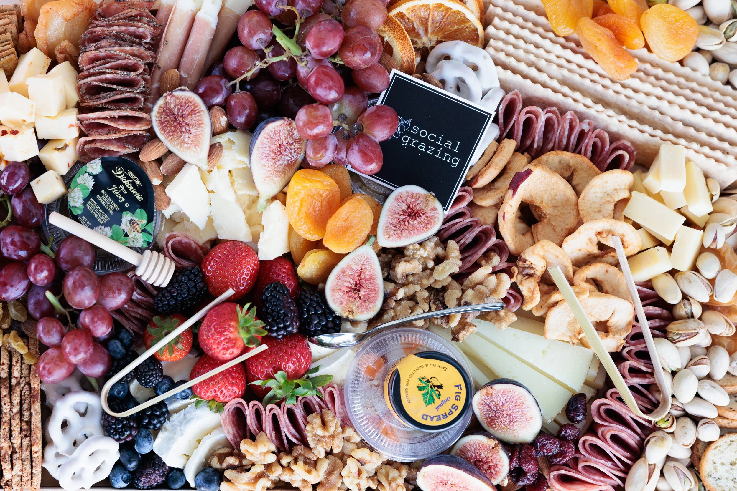 Assorted charcuterie board with cheeses, grapes, strawberries, blackberries, dried apricots, figs, assorted meats, nuts, crackers, dried apple slices, and honey.
