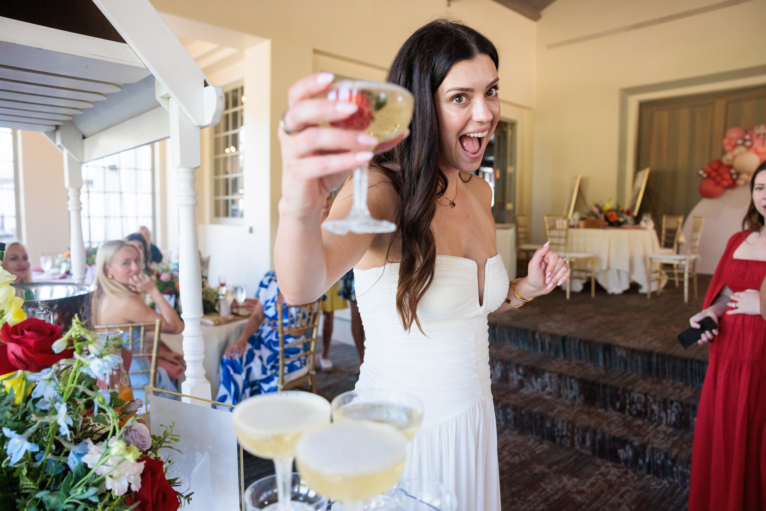 A woman in a white dress holding a cocktail and smiling at a celebration or party.