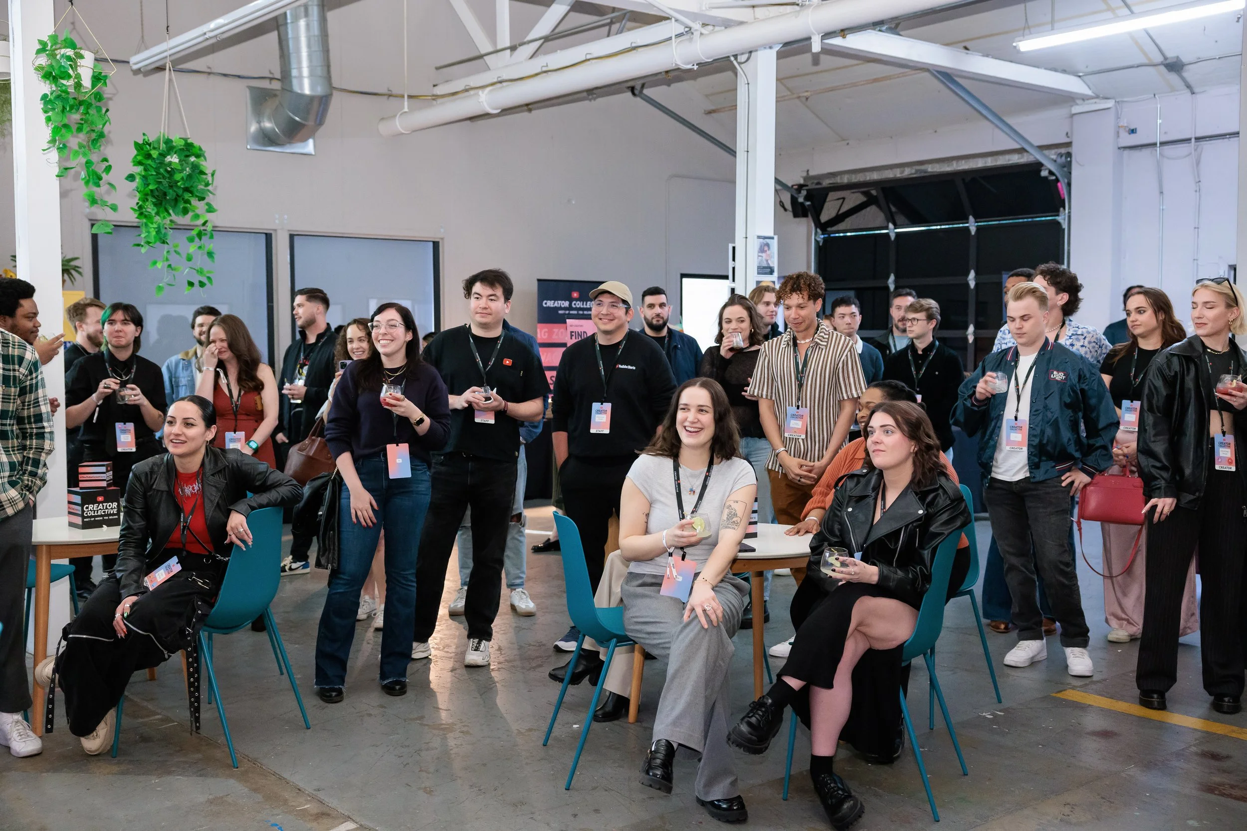 Group of diverse people at an indoor event, some sitting and some standing, engaging and smiling, with drinks in hand.