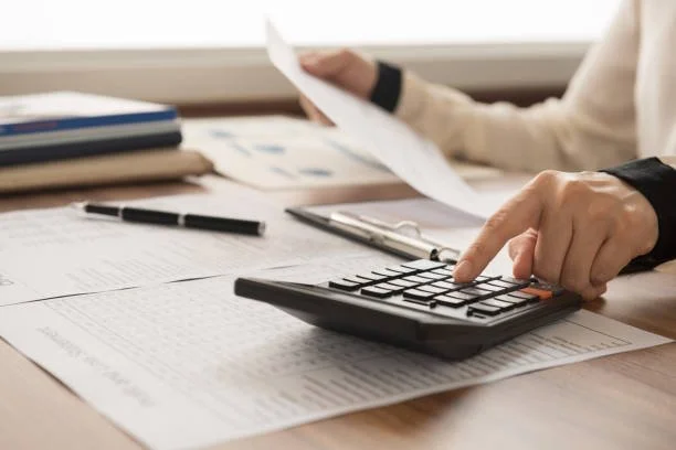 Person using a calculator and reviewing documents at a desk in an office.