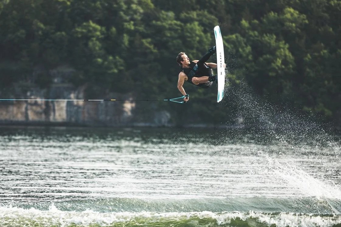 Wakeboard World Champion and owner of Kirby's School of Wake, Kirby Liesman flying high on a wakeboard high above the water with a wooded shoreline in the background.