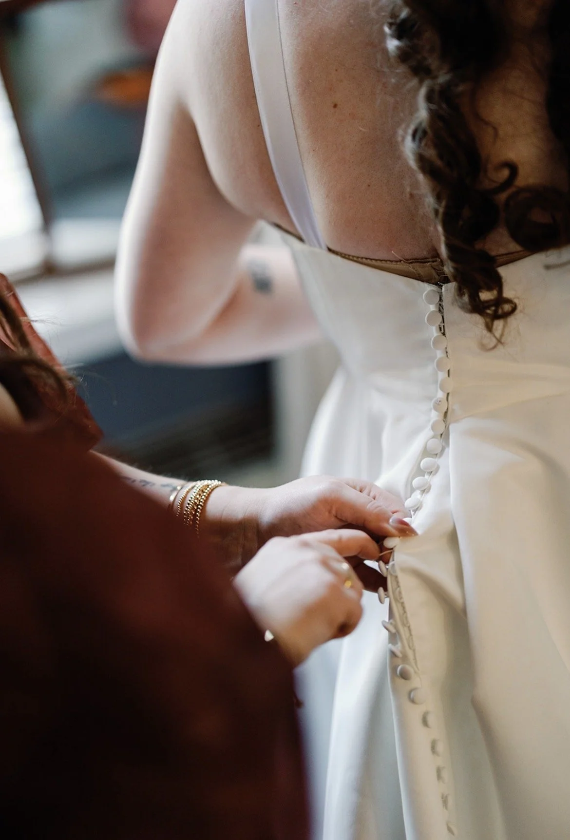 A person helping a bride button her wedding dress.