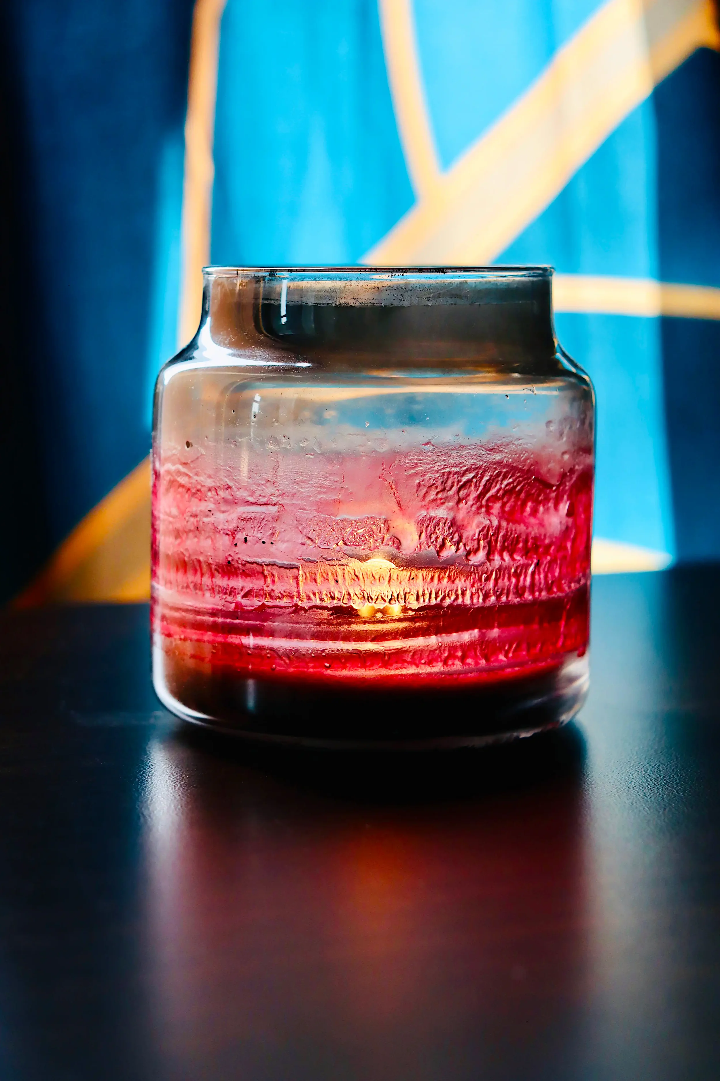 Glowing red candle in a textured glass jar