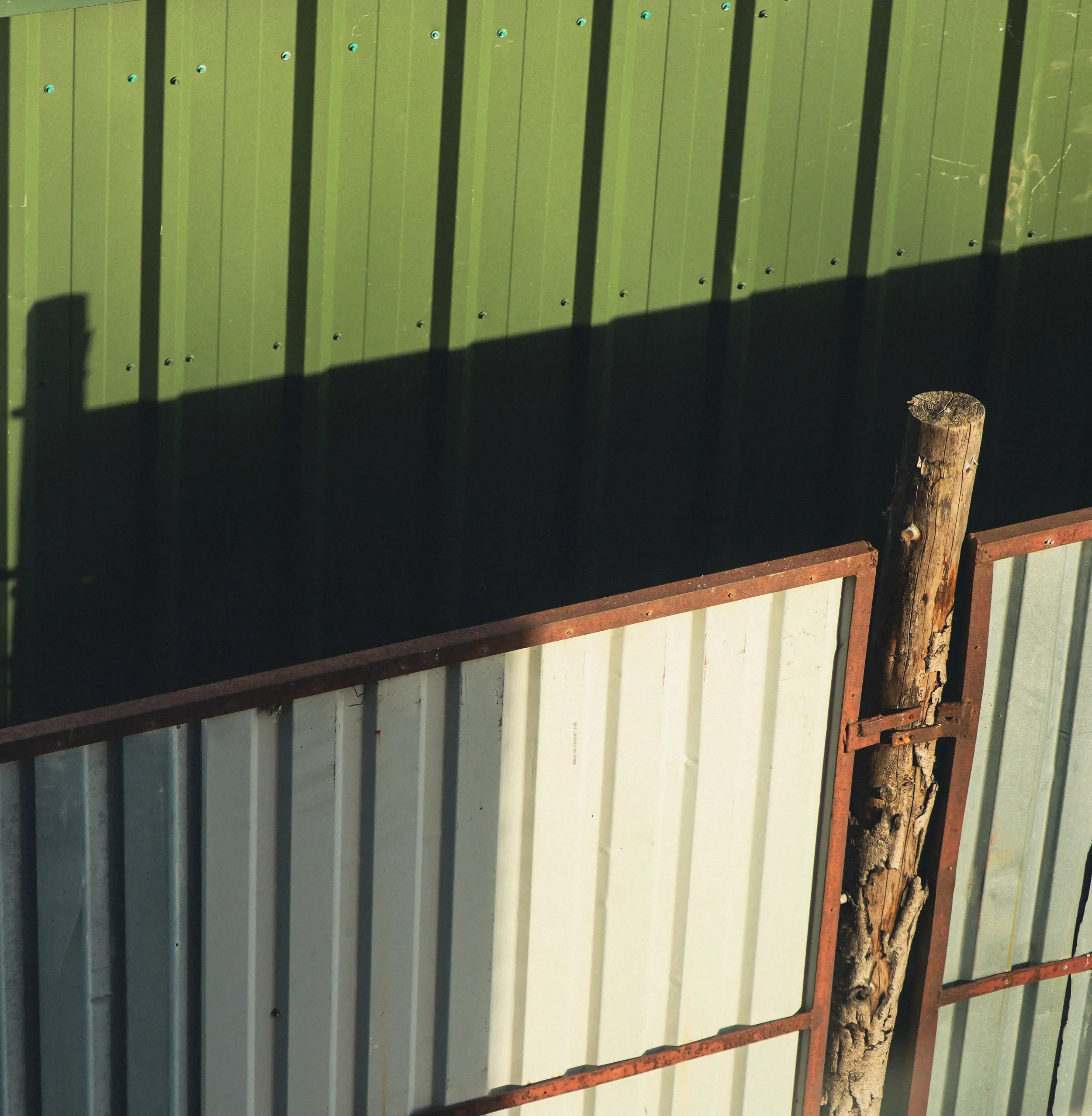 Green corrugated metal wall with rusty frame and weathered wooden post