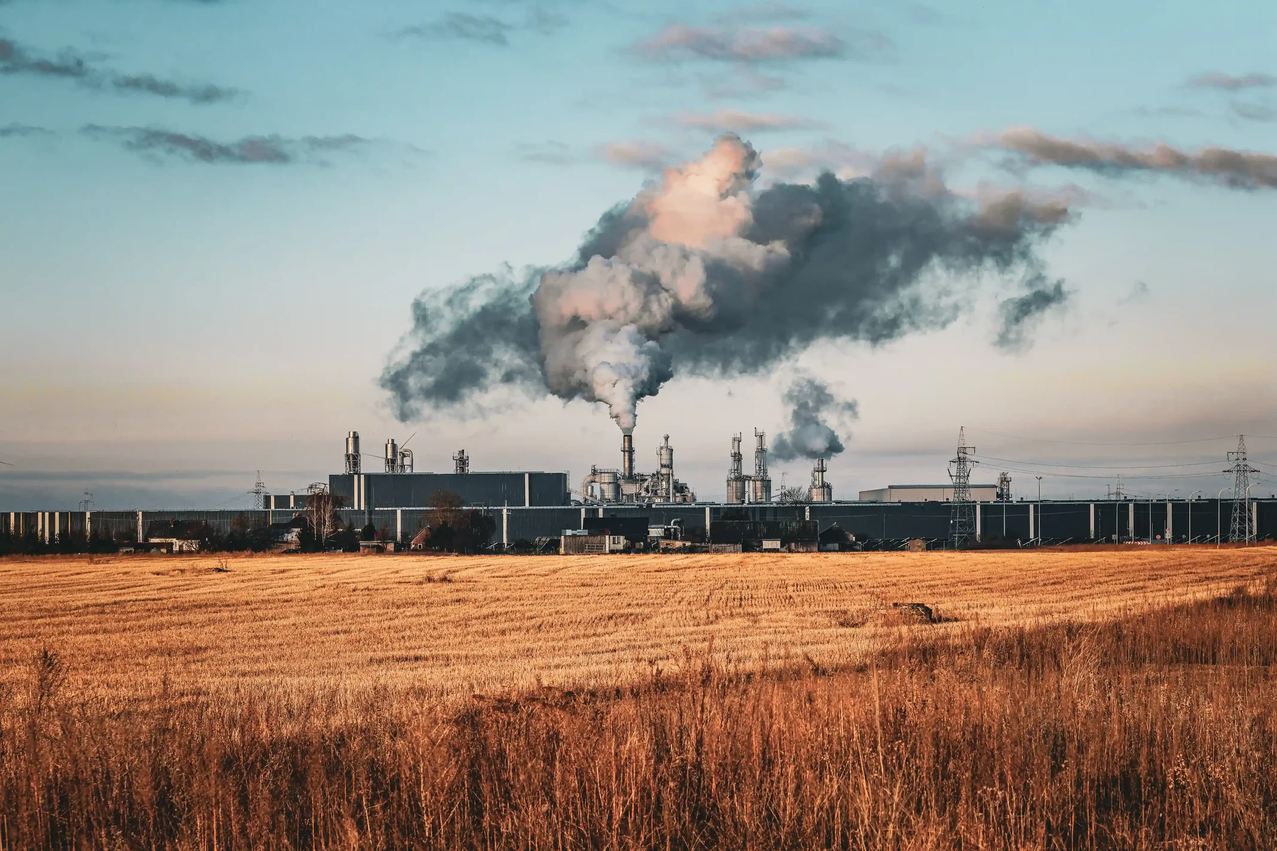 Factory smokestacks releasing smoke above a dry field at golden hour