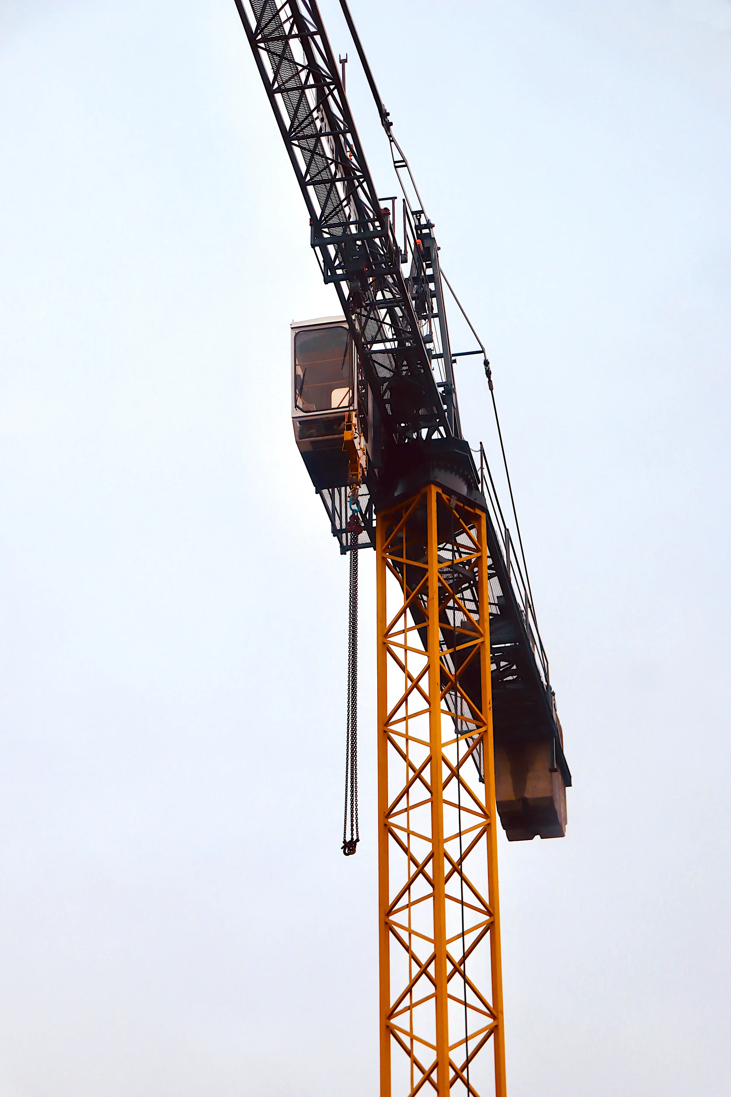 Yellow tower crane with hanging chains against an overcast sky