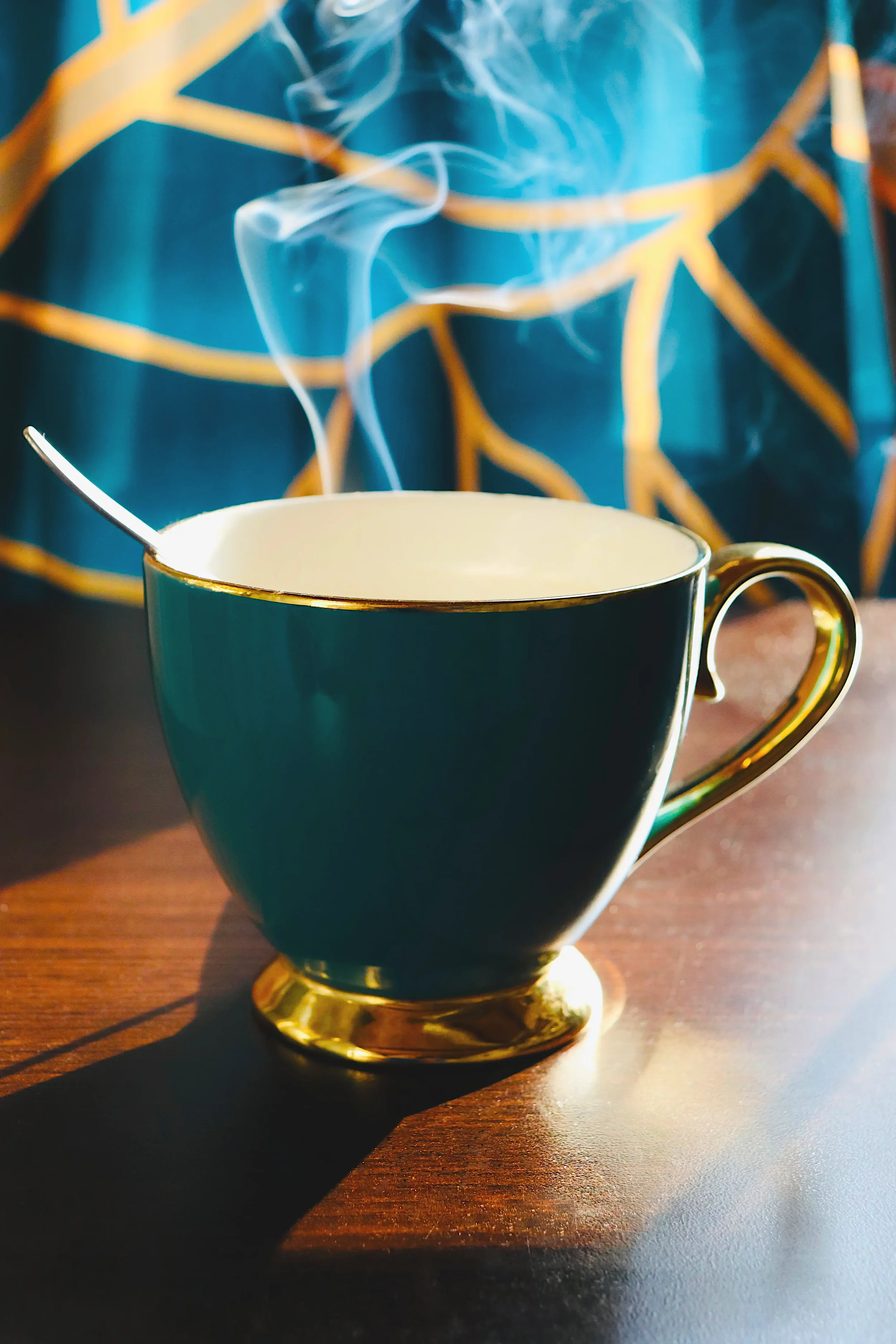 Teal teacup with spoon on a dark wooden table in window light