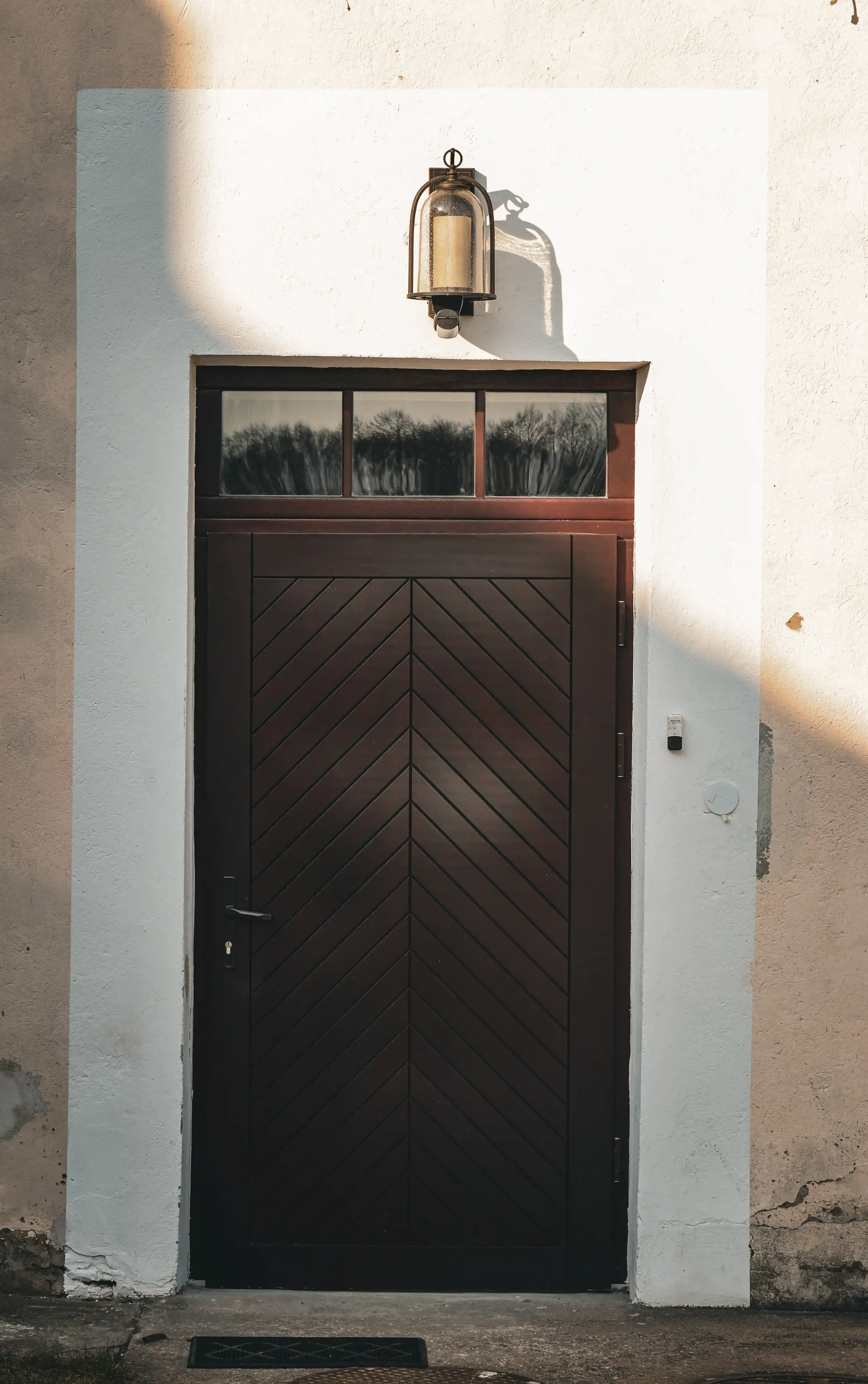 Dark wooden chevron-pattern door with transom window and vintage lantern
