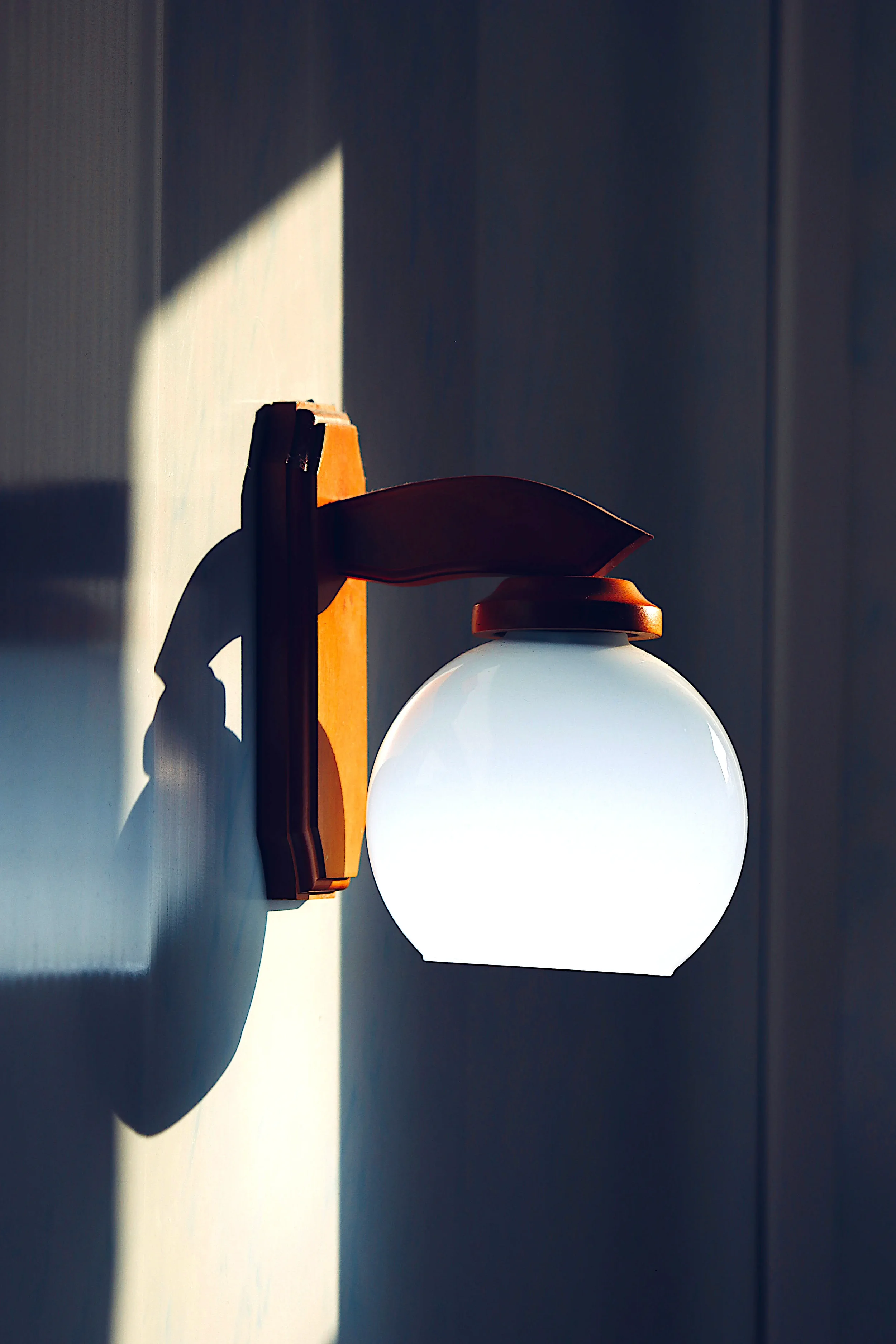 Wooden wall sconce with white glass globe casting a shadow on the wall