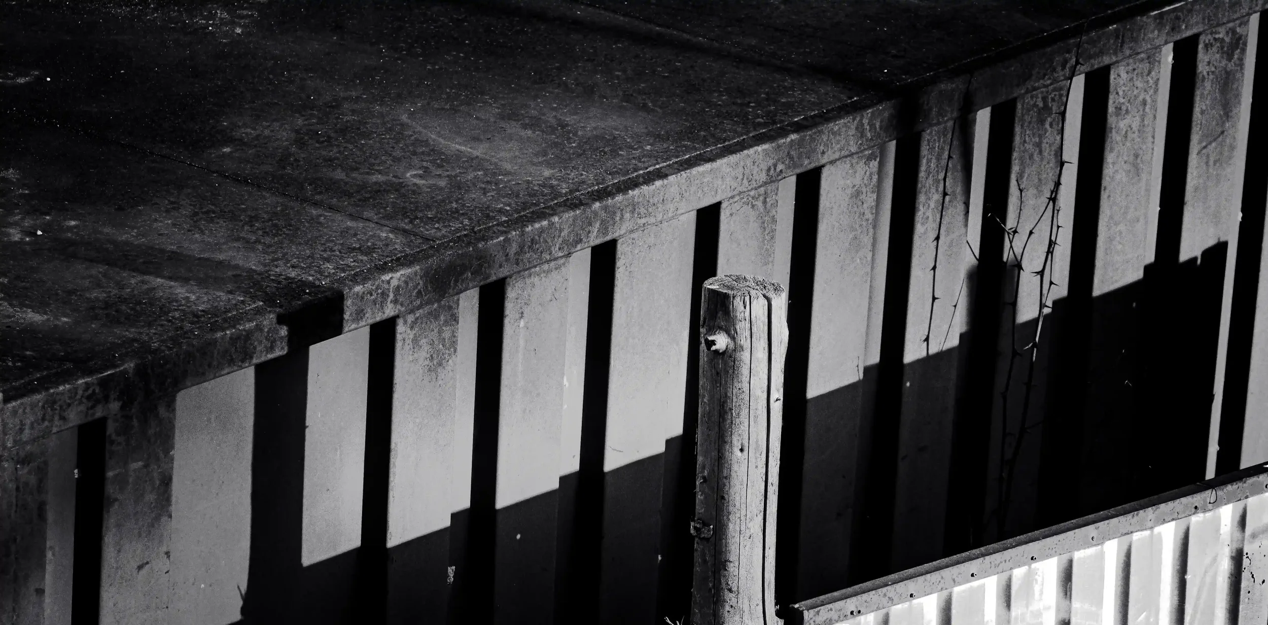 Black and white detail of a weathered wooden post and metal panels