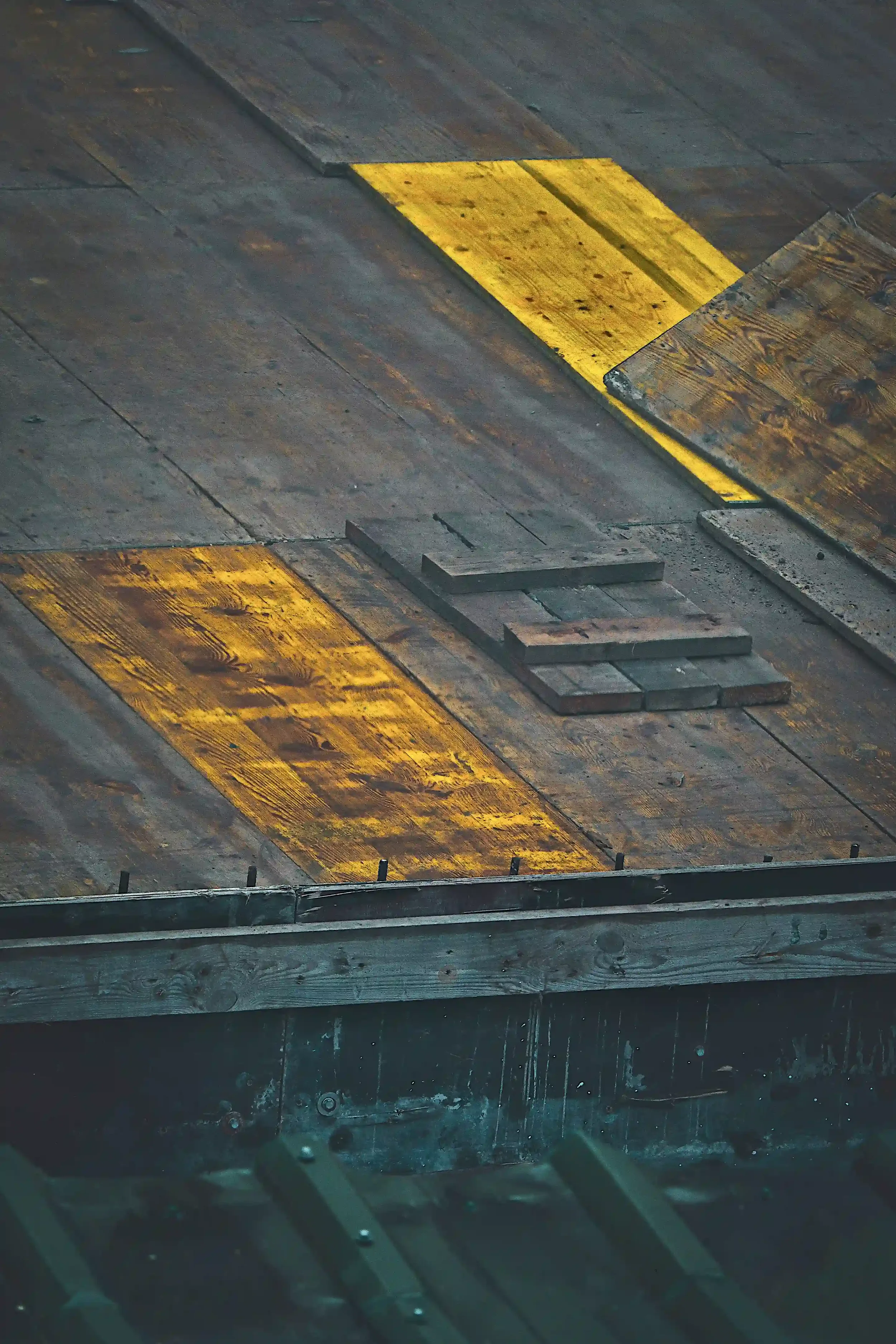 Weathered wooden planks with yellow painted sections and strong shadows