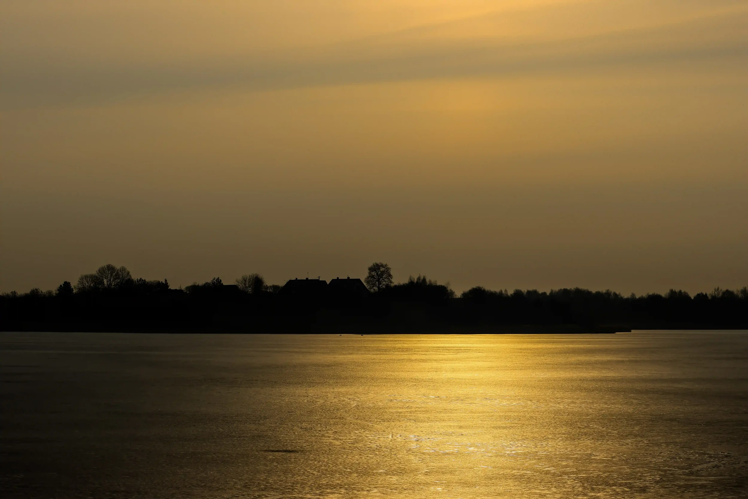 Frozen lake with golden reflection and distant silhouetted shoreline