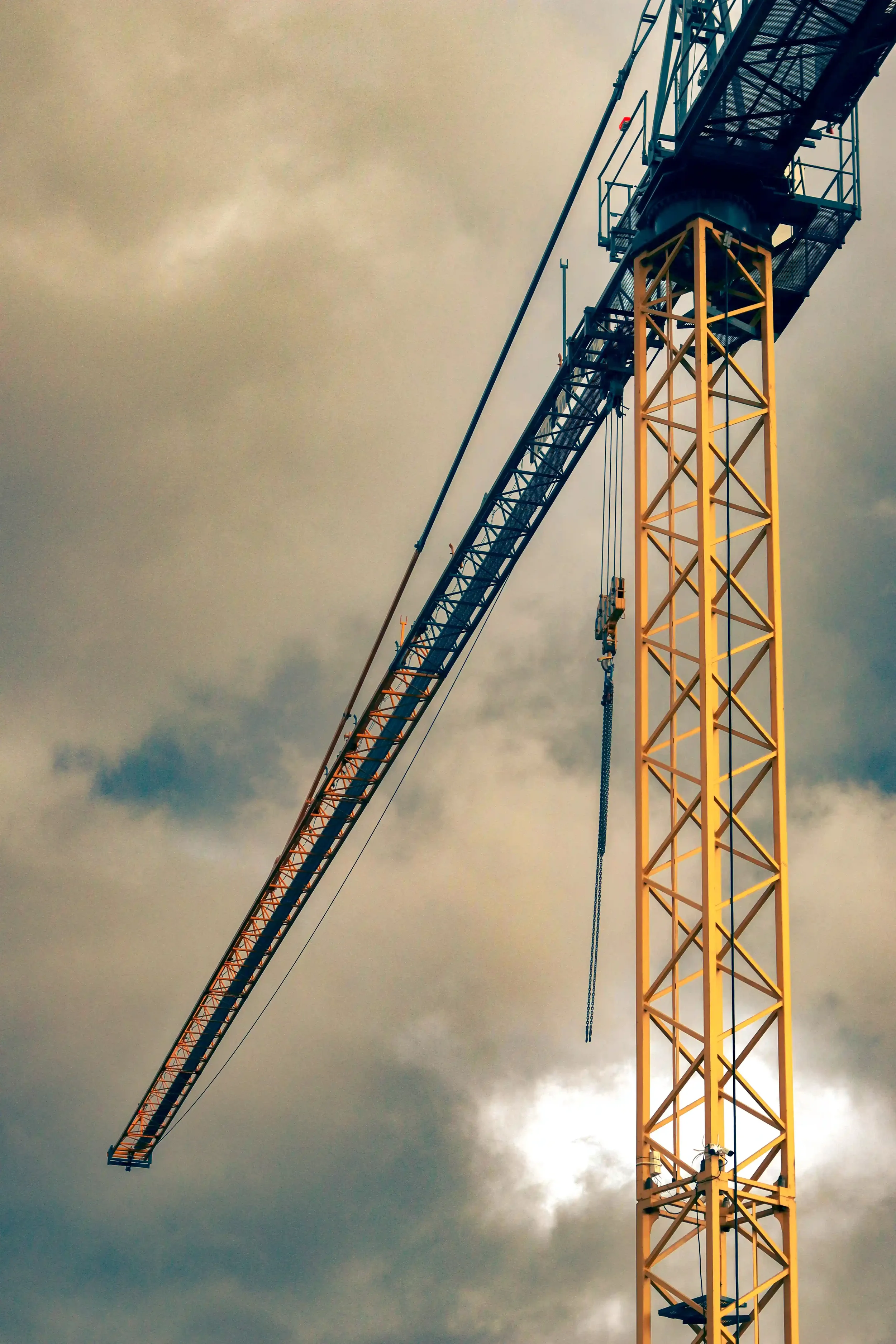 Yellow and teal tower crane against a cloudy sky