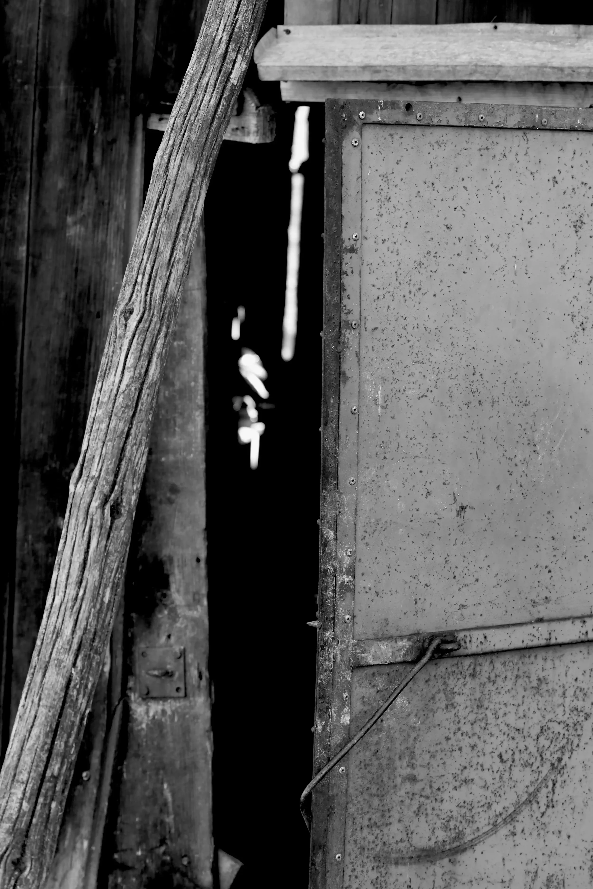 Black and white detail of a weathered wooden beam and riveted metal panel