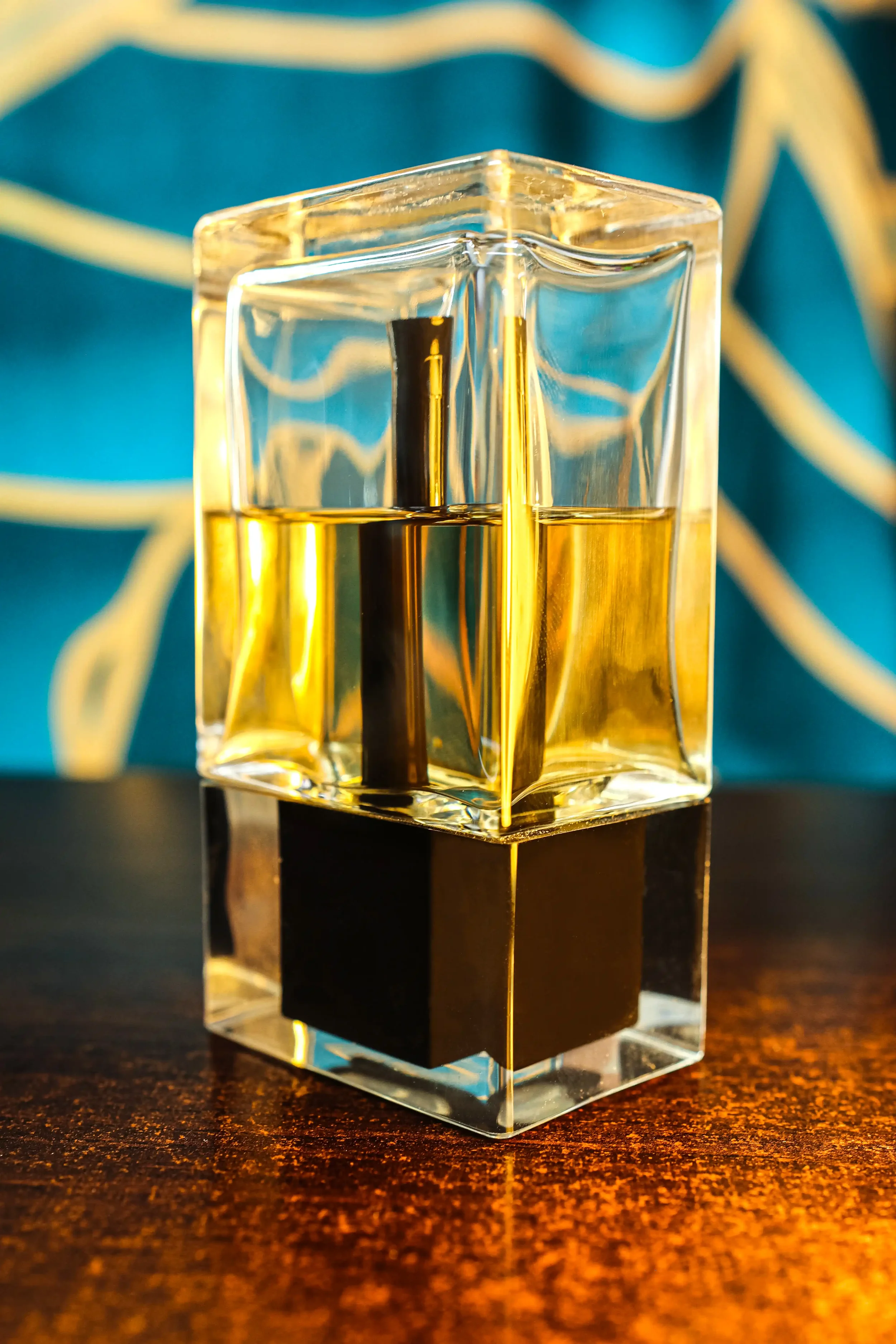 Square glass bottle with golden liquid and black base on a dark wooden surface