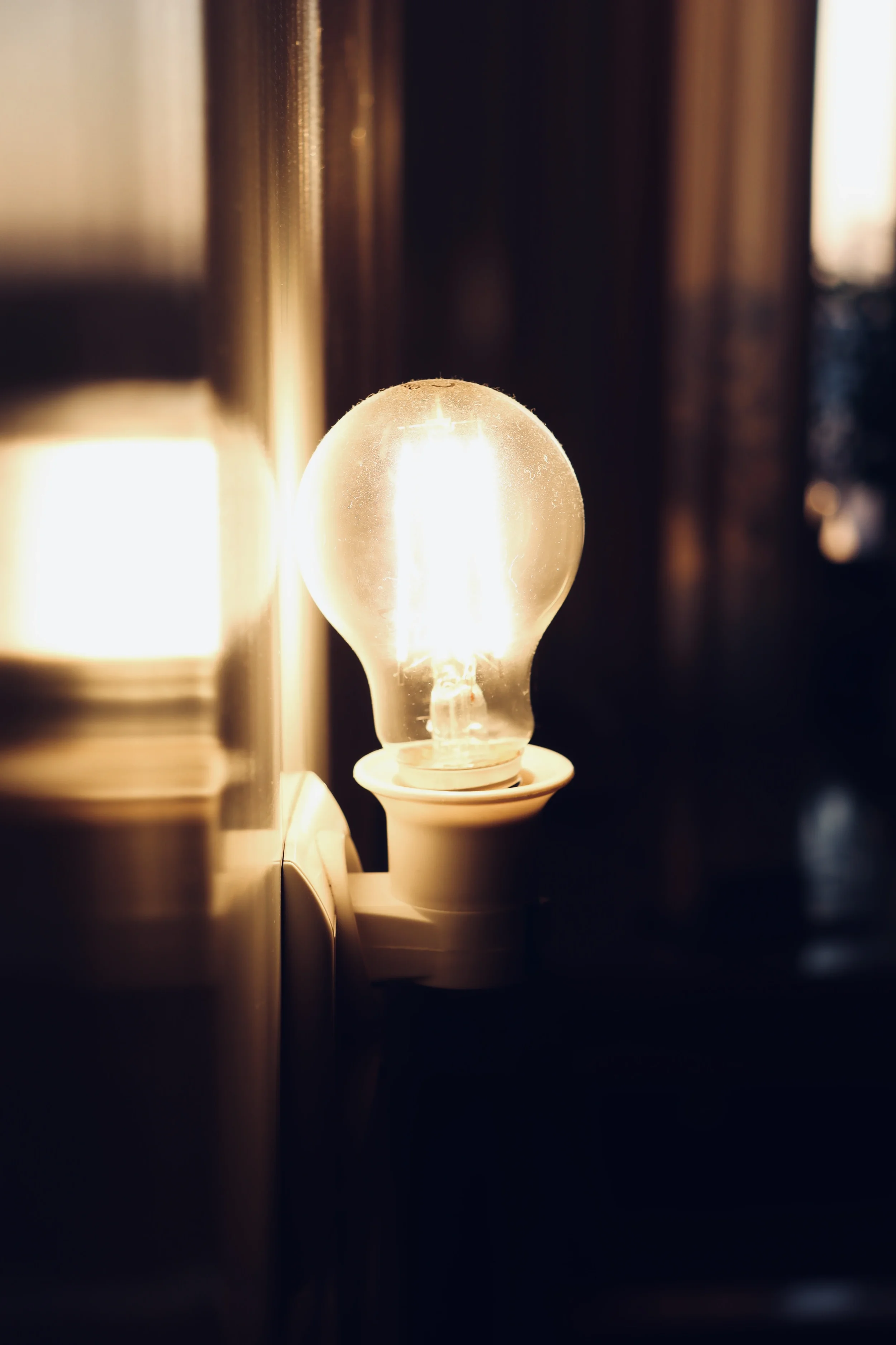 Glowing light bulb attached to a wall socket in a dim room