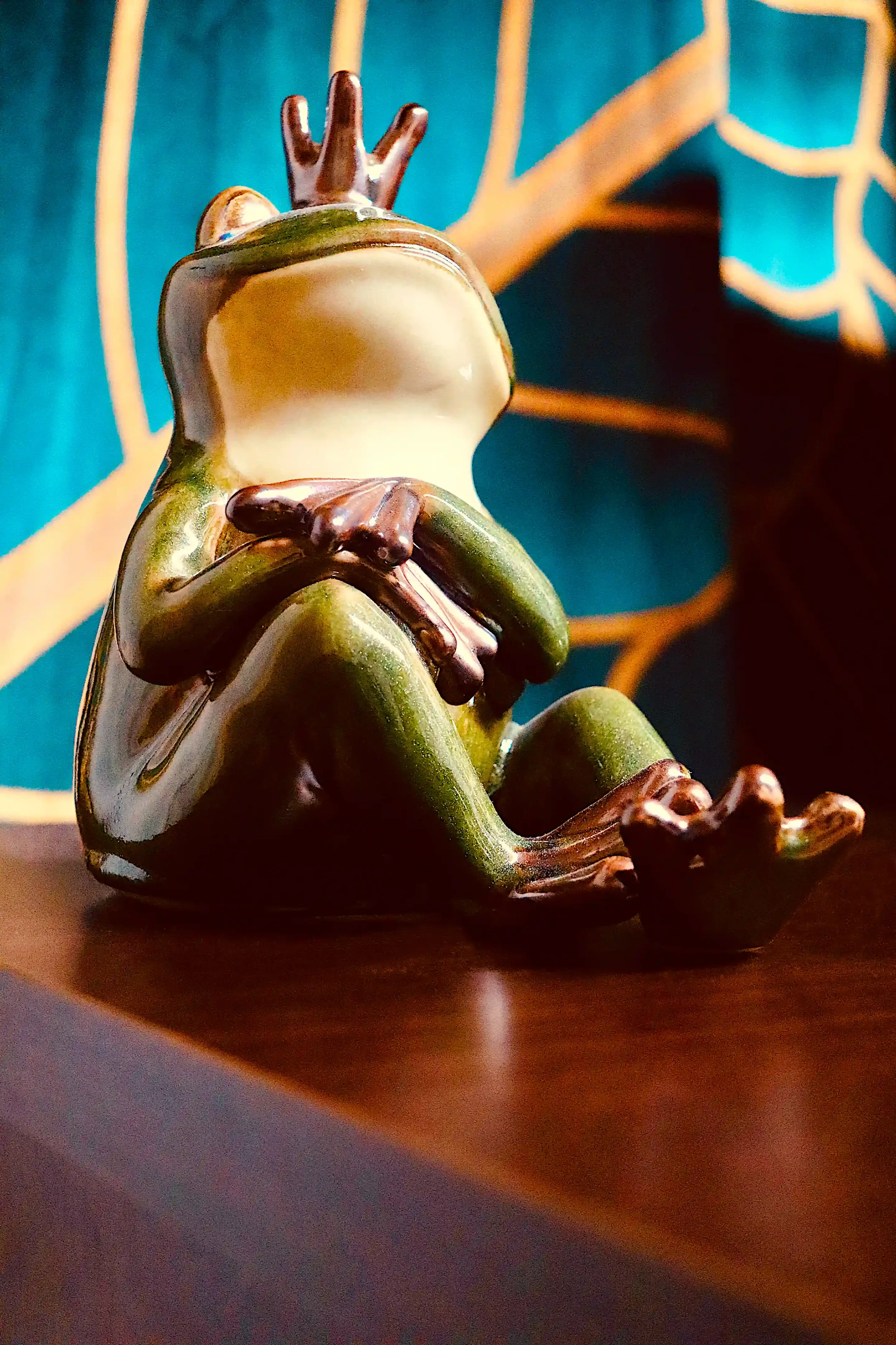 Green ceramic frog figurine with brown crown on a dark wooden surface
